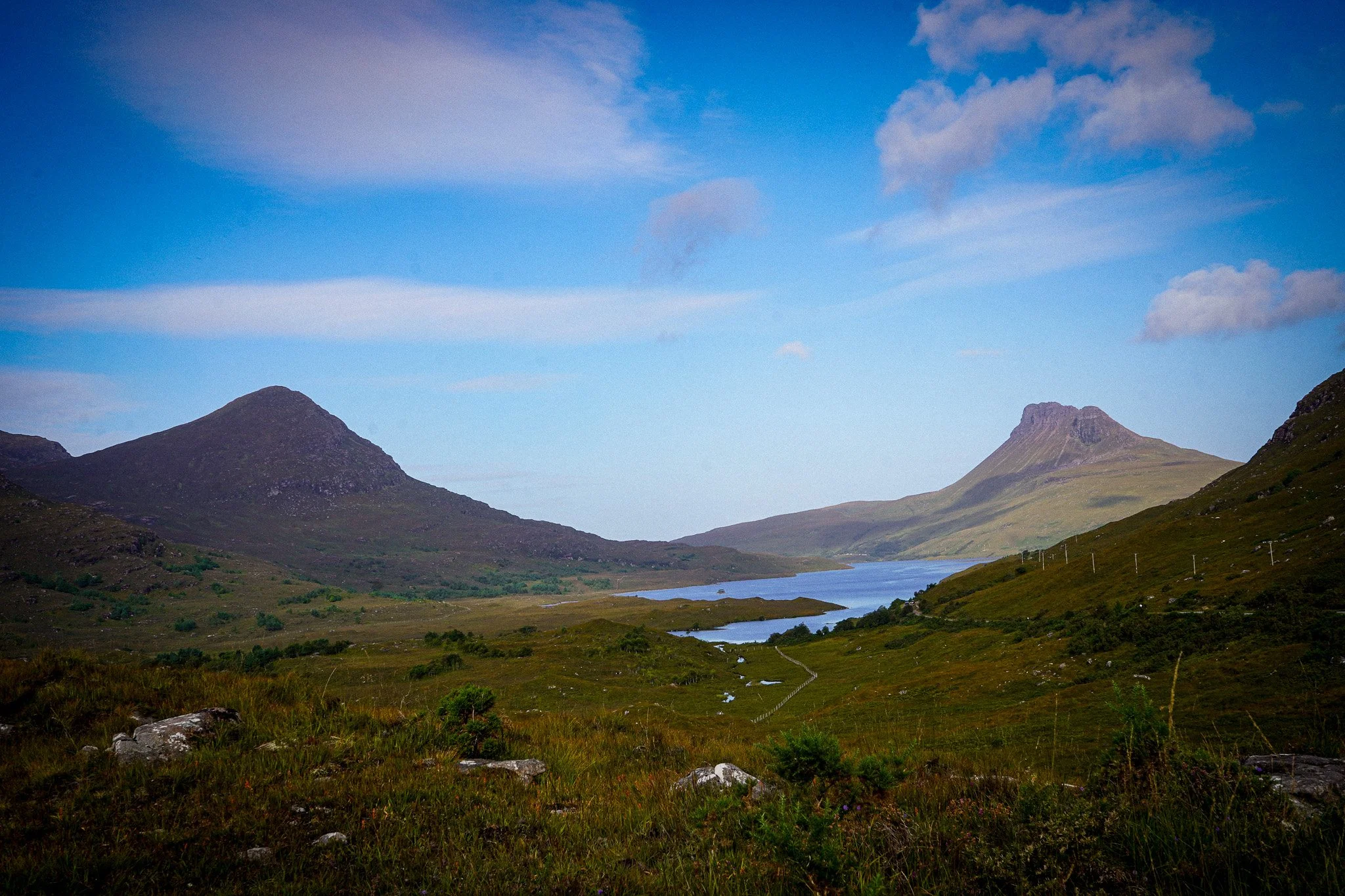 Scenic landscape with mountains, a river flowing through the valley, and a blue sky with scattered clouds.