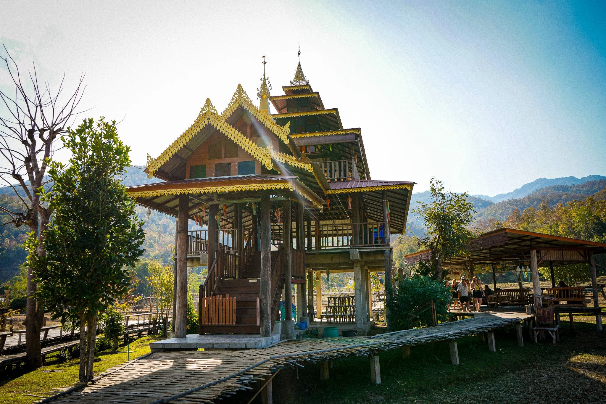 Traditional wooden watchtower with ornate golden roofs in a rural setting with mountains in the background.