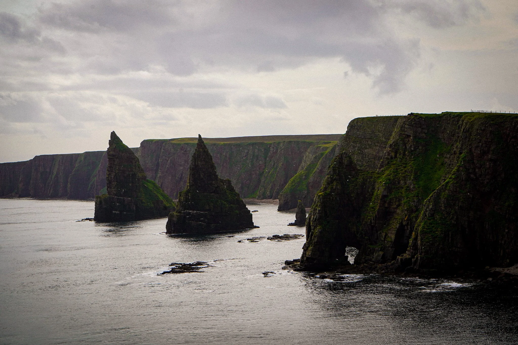 Cliffs and sea stacks along a rugged coastline under a cloudy sky.