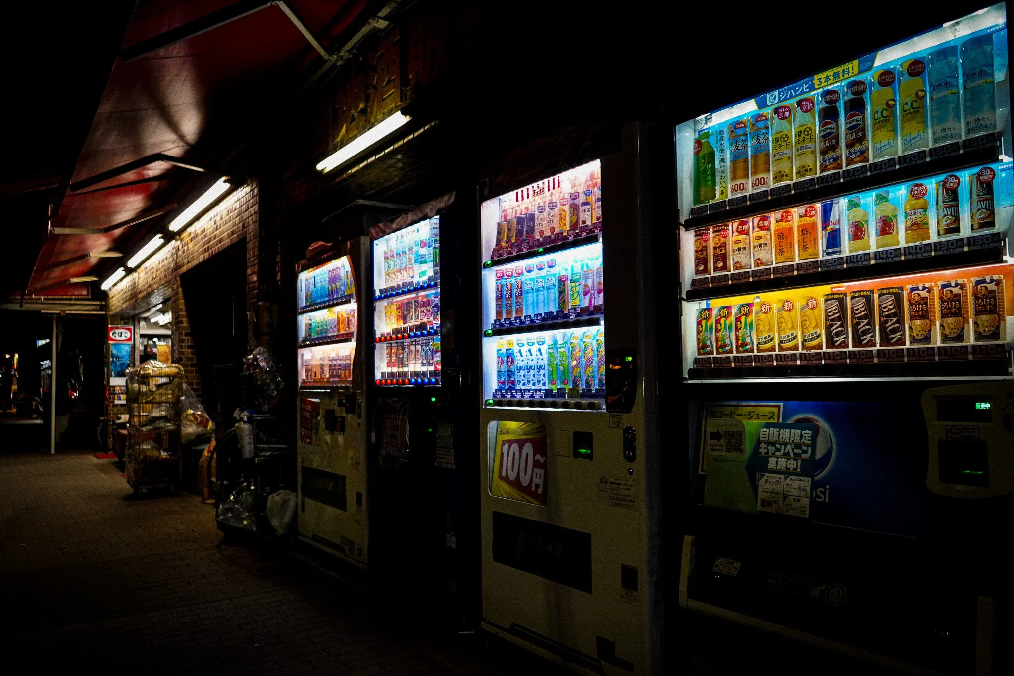 Vending machines selling drinks and snacks under a dark, covered area at night.