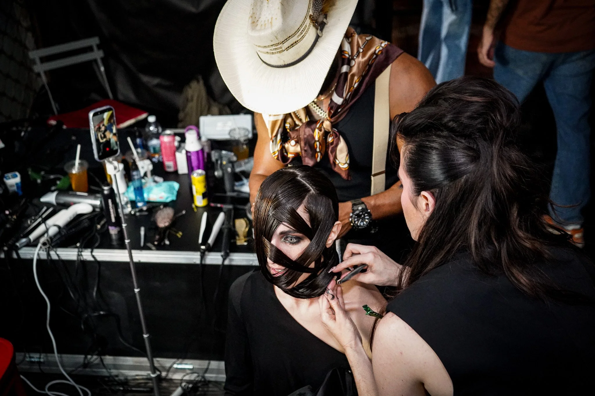 A model getting her hair styled at a salon station with various hair styling tools and products on the table in front of her.