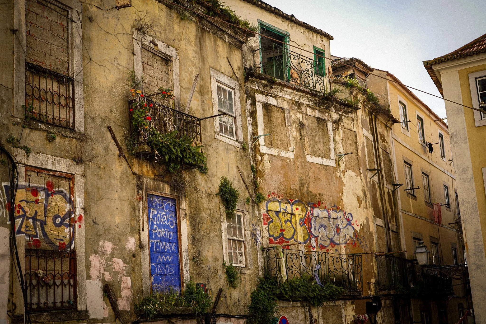 An old, weathered building with graffiti and plants on the balcony, showing signs of decay and neglect.