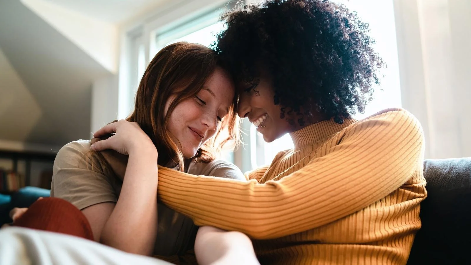 Two people embracing on a couch with their foreheads touching, sharing a moment of emotional connection.