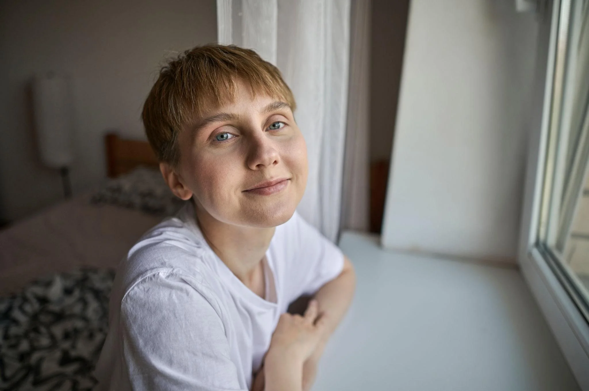 Person in a white T-shirt smiling softly at the camera, conveying warmth and self-acceptance.