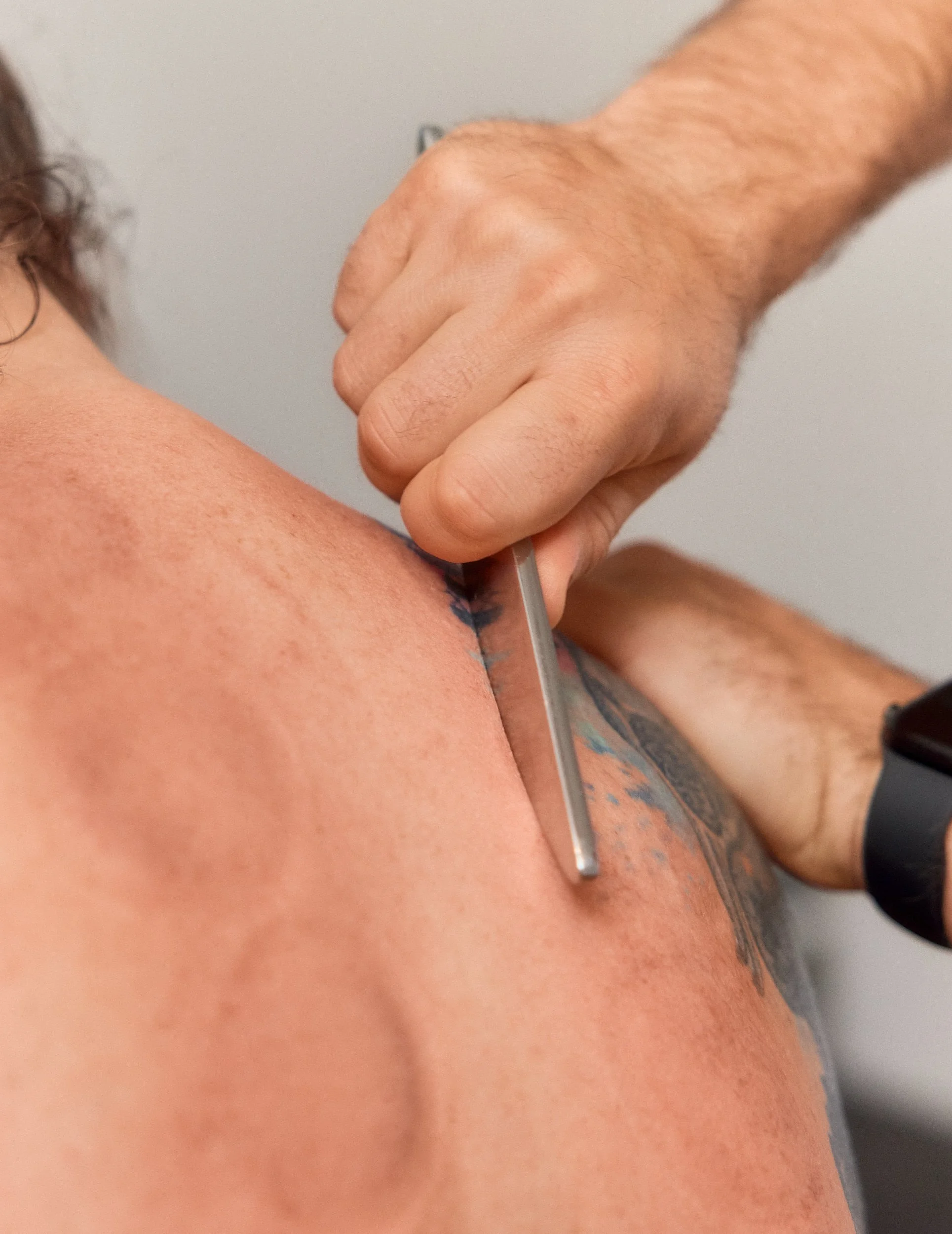 Masseur führt eine Rückenmassage an einem Kunden aus, sichtbarer Tattoo auf Rücken, in einer Behandlungsszene.