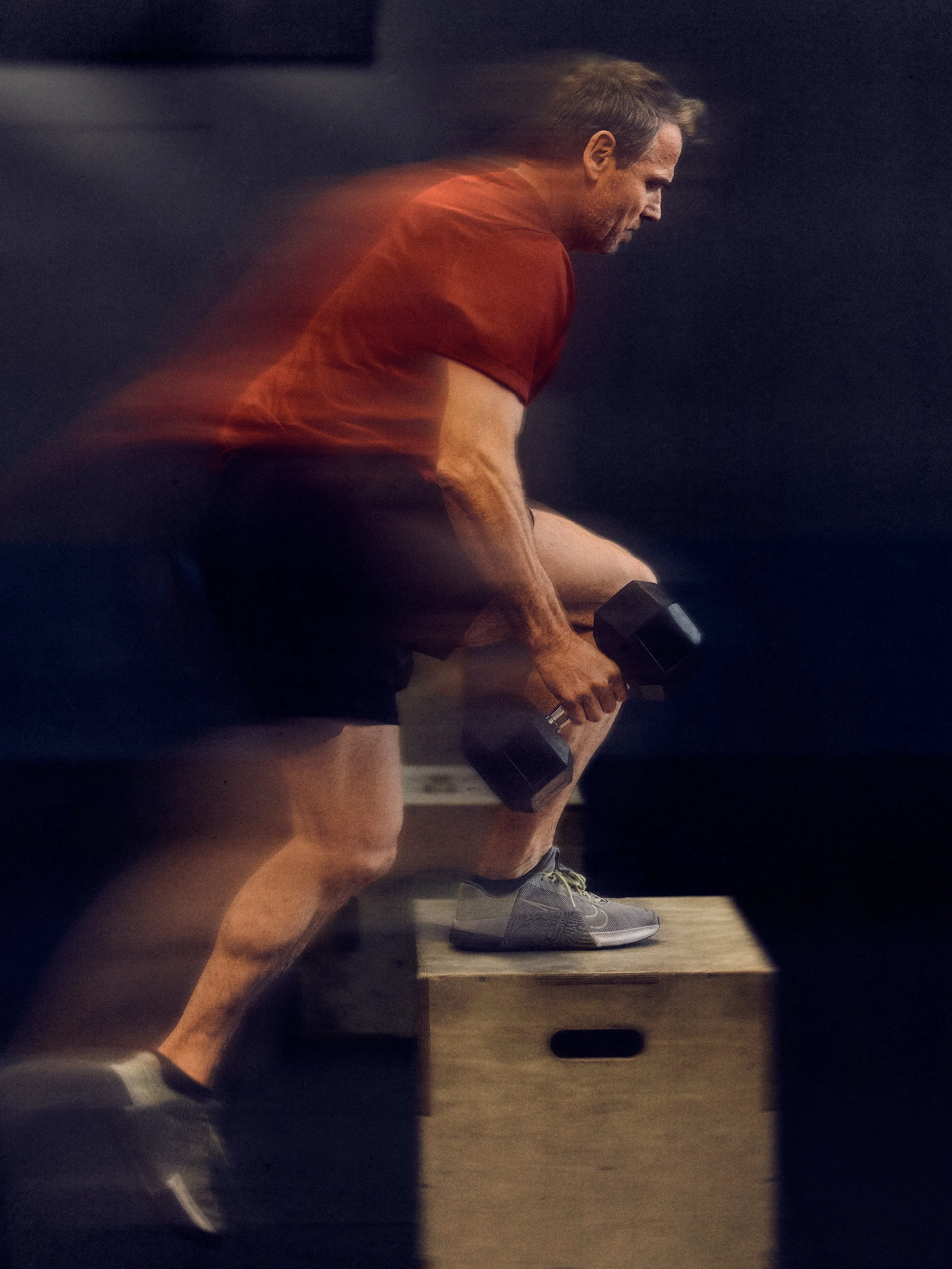 Ein Mann trainiert mit Hanteln auf einem Holzpodest in einem Fitnessraum.