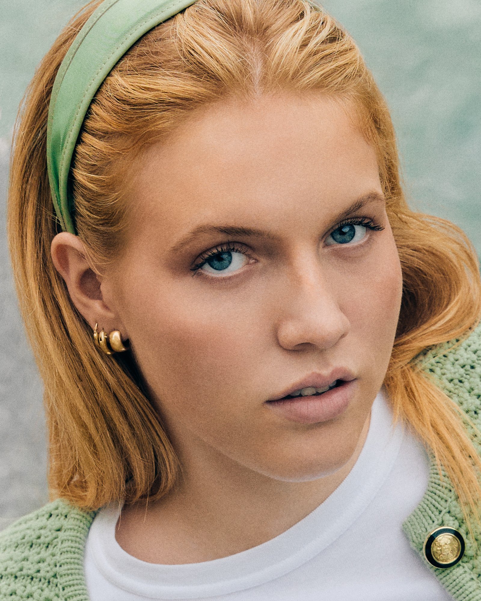 Fotograf & Videograf Wil SG | Businessfotografie Ostschweiz Daniel Dorrer Nahaufnahme eines jungen Mädchens mit blonden, lockigen Haaren, blauen Augen und Ohrringen, trägt eine grüne Strickjacke