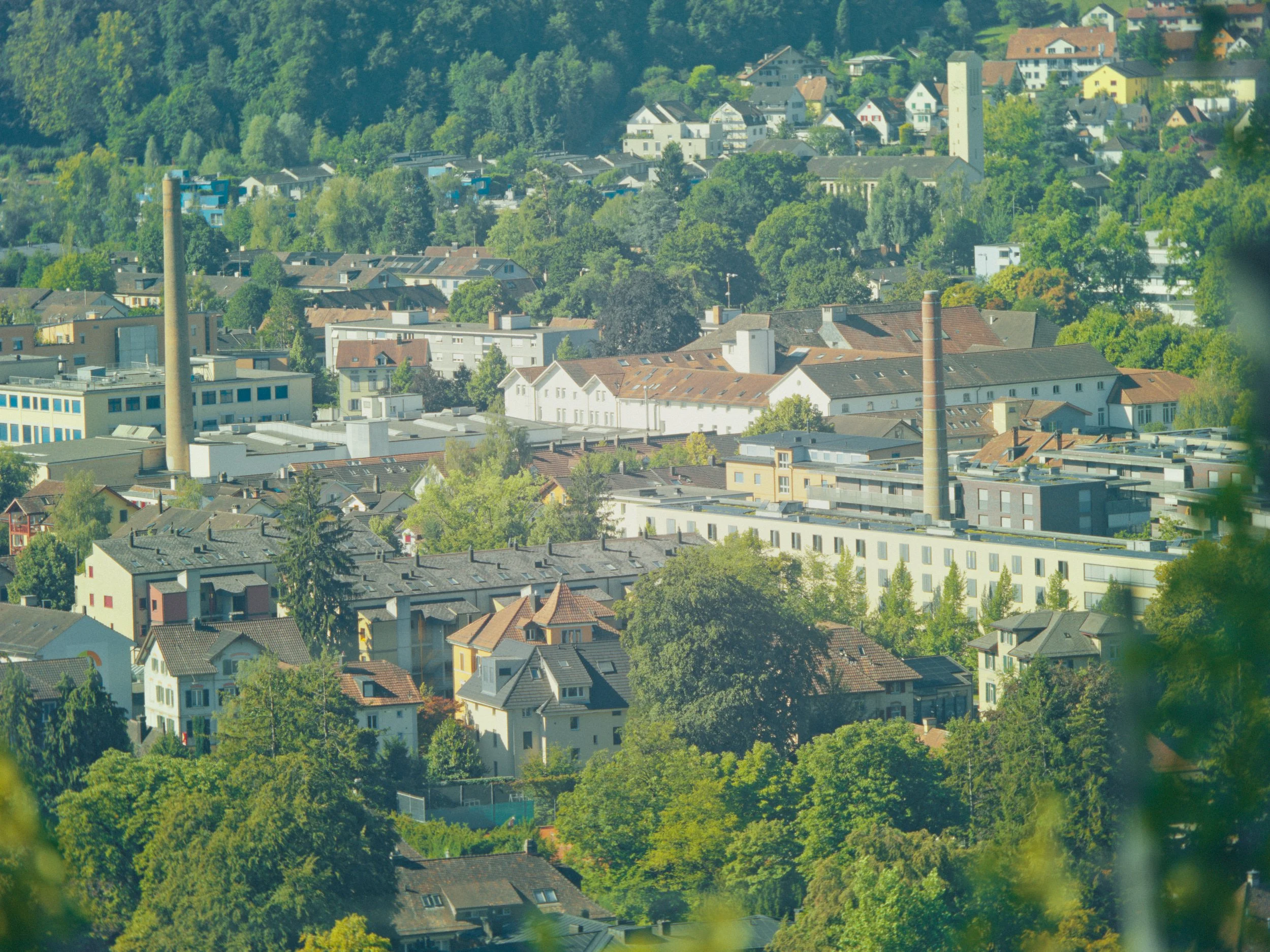 Luftaufnahme eines Stadtviertels mit vielen Häusern, Bäumen und Hügeln im Hintergrund, Sommerzeit.