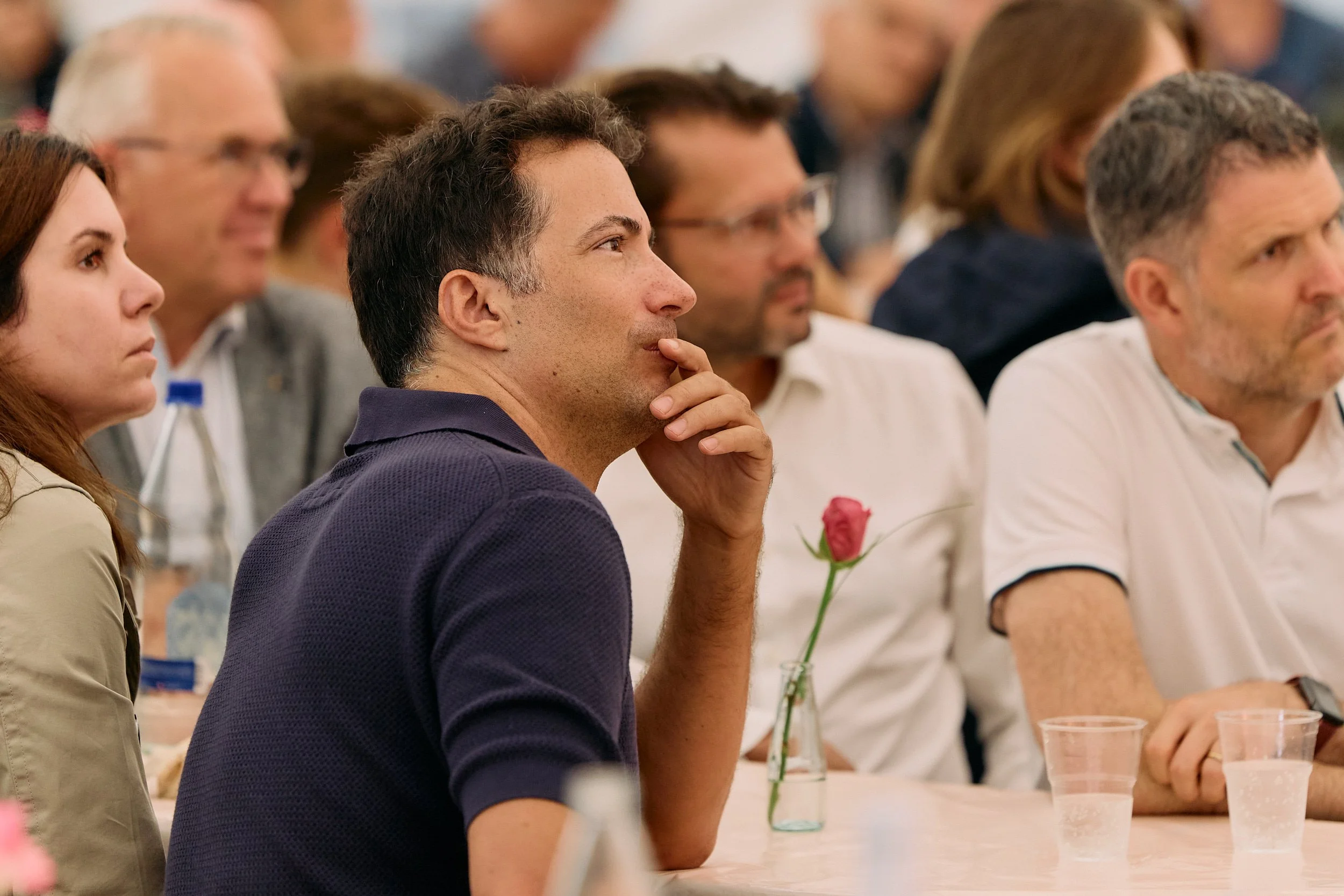 Menschen sitzen bei einem Treffen oder Vortrag an einem Tisch, einige sehen nach vorne. 100 Jahre Gymnasiums Friedberg Gossau SG.