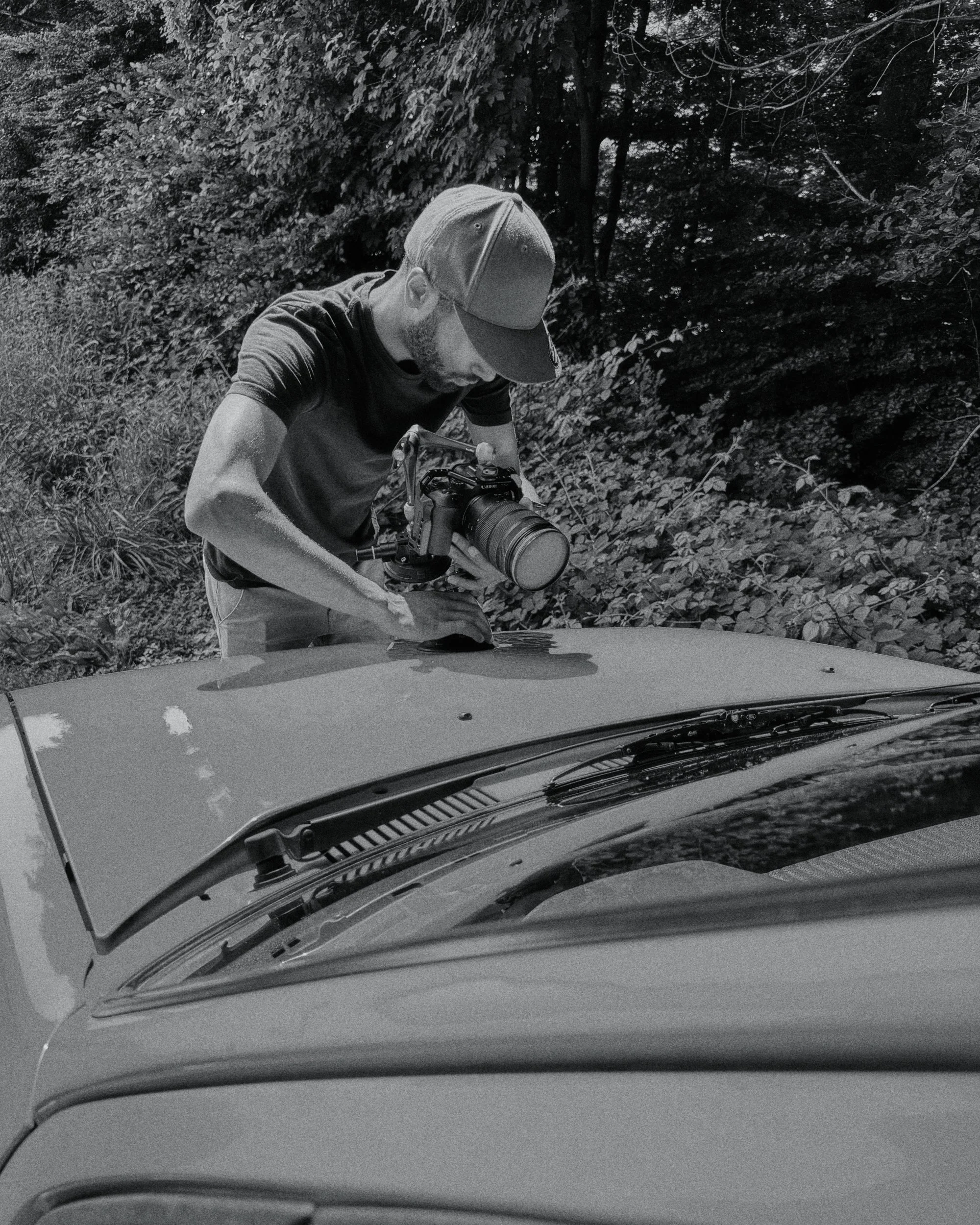 Mann mit Baseballcap fotografiert einen Auto auf einer landlichen Straße im Wald, schwarzen und weißen Foto.