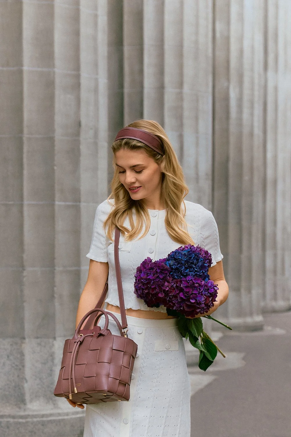 Fotograf & Videograf Wil SG | Businessfotografie Ostschweiz Daniel Dorrer Eine junge Frau mit blonden Haaren trägt eine weiße, kurze Jacke und einen weißen Rock, hält einen Blumenstrauß aus blauen und violetten Hortensien und trägt