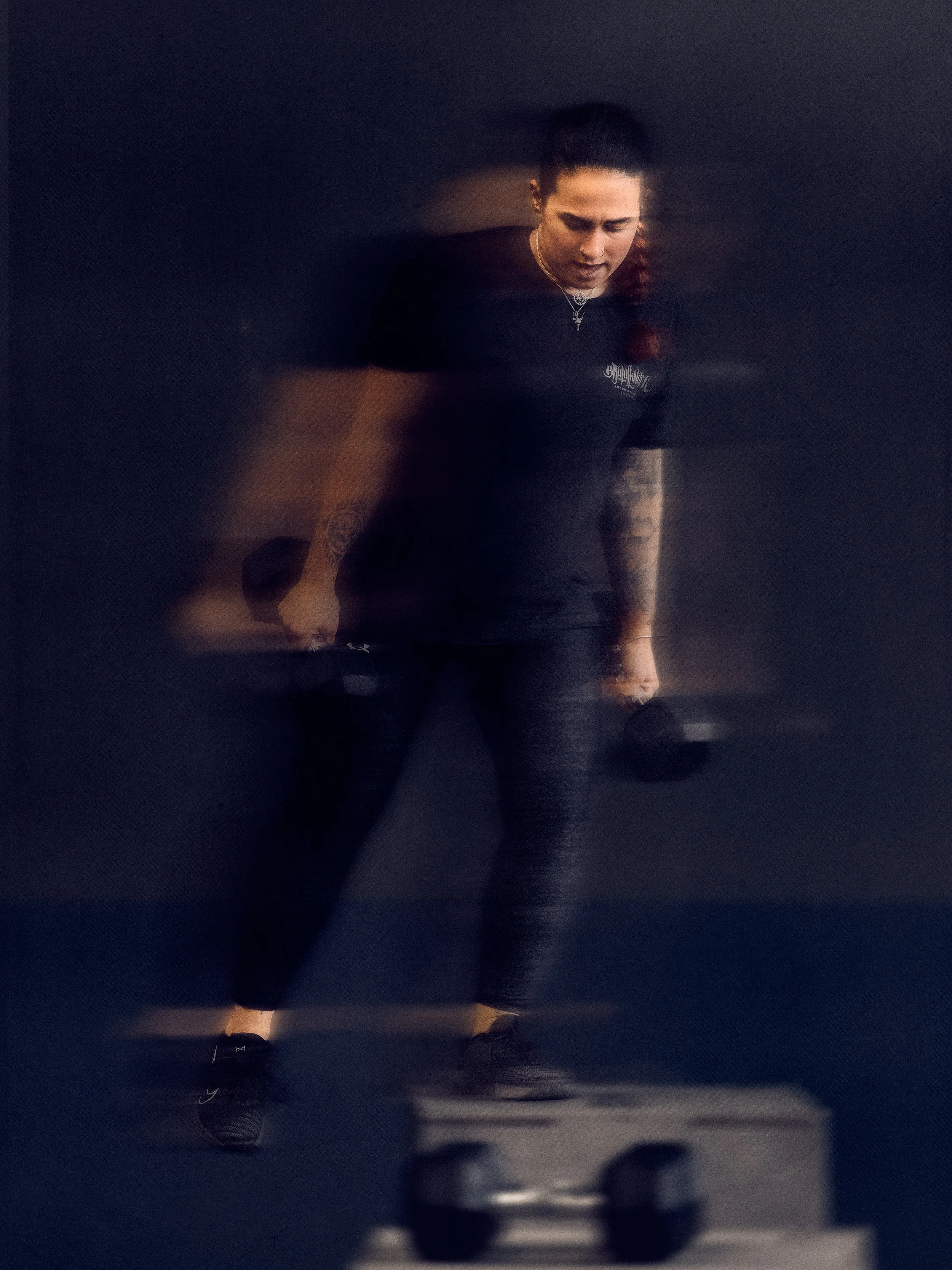 Eine Frau beim Krafttraining, die in die Hocke geht, mit Hanteln in den Händen, auf einem dunklen Trainingsboden in einem Fitnessstudio.