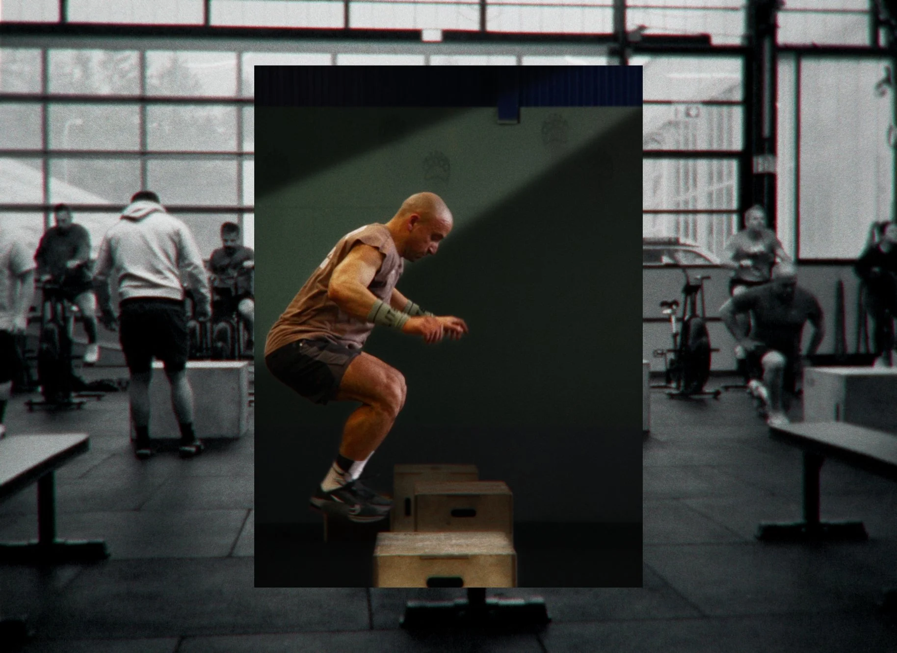 Mann springt beim Boxtraining auf eine Kiste in einem Fitnessstudio mit weiteren Trainierenden im Hintergrund.