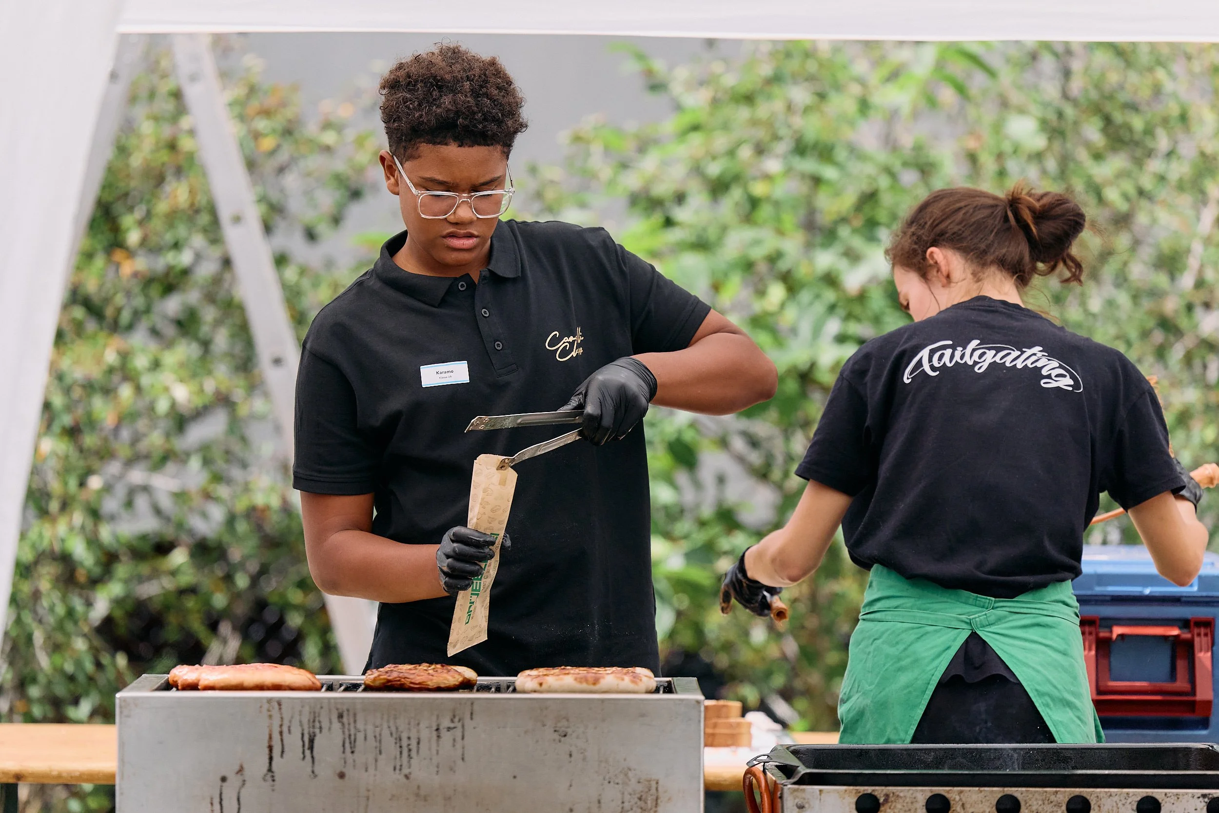 Fotograf & Videograf Wil SG Ostschweiz Daniel Dorrerlegt Fleisch auf den Grill, während die andere Person neben dem Grill steht. 100 Jahre Gymnasiums Friedberg Gossau SG.