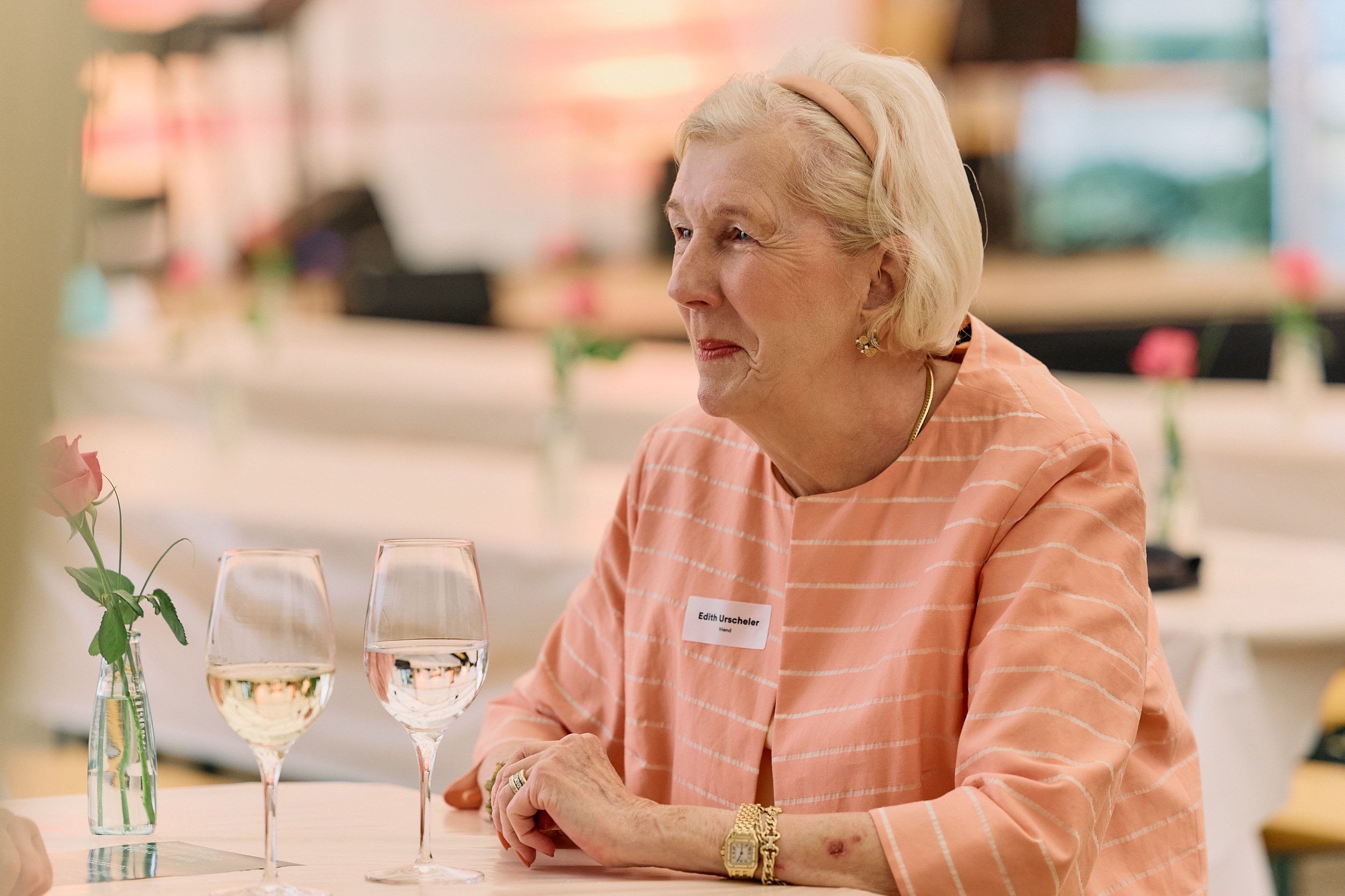 Fotograf & Videograf Wil SG | Businessfotografie Ostschweiz Daniel Dorrer Eine ältere Frau mit blondem Haar, die an einem Tisch sitzt, trinkt Wein. 100 Jahre Gymnasiums Friedberg Gossau SG.