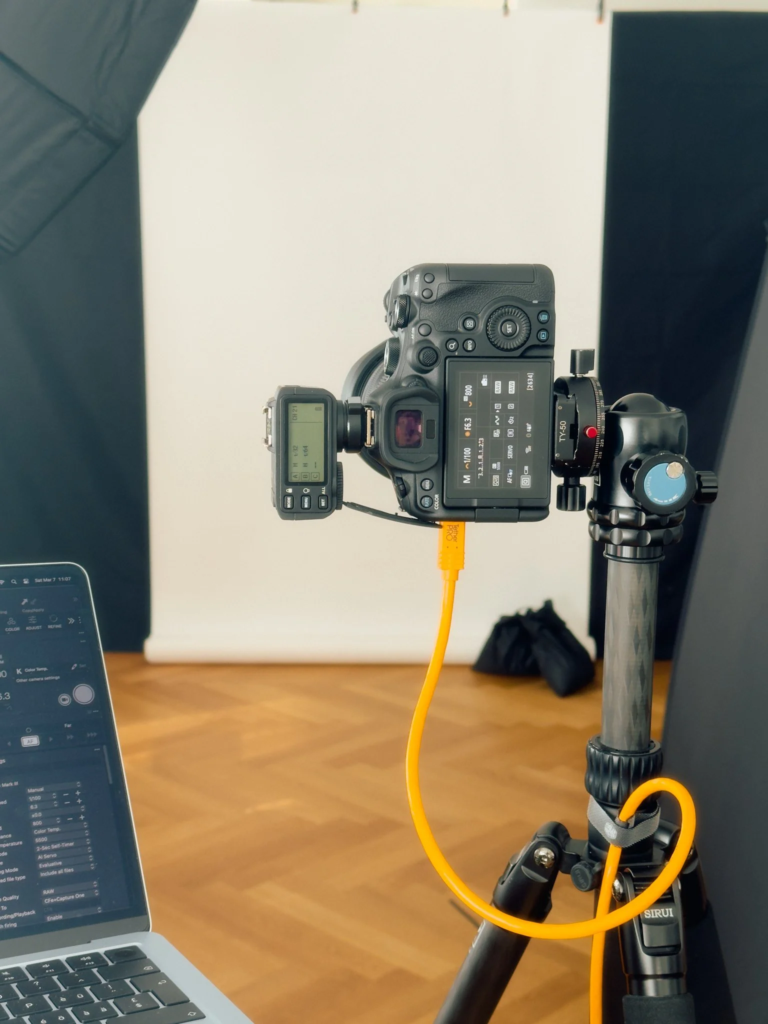 Eine Kamera ist auf einem Stativ montiert und auf einen Laptop gerichtet, in einem Fotostudio mit Hintergrund. Das Bild zeigt eine professionelle Ausrüstung in einem Aufnahmestudio.