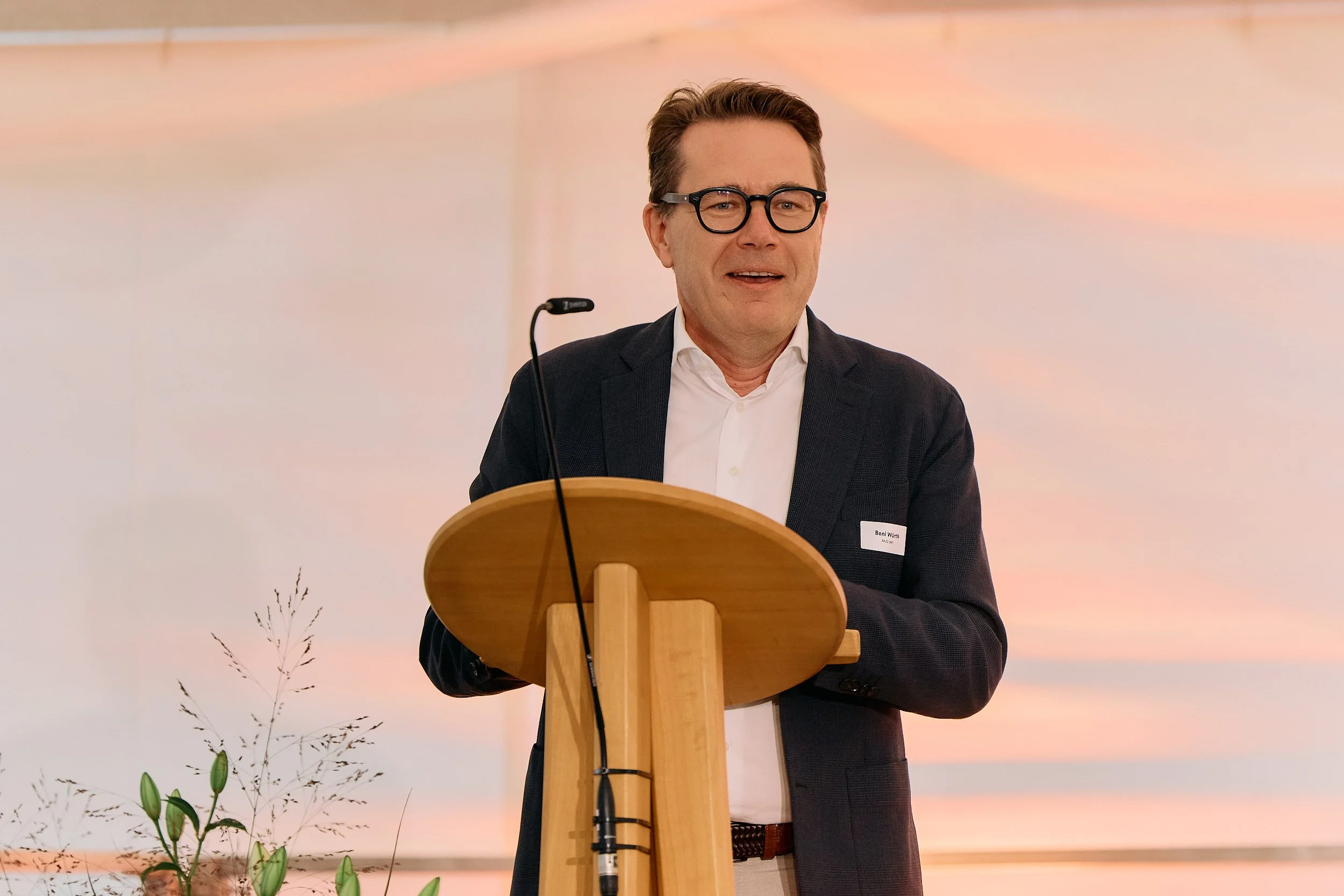 Fotograf & Videograf Wil SG Ostschweiz Daniel DorrerEr trägt eine dunkle Jacke, eine weiße Hemd und trägt eine Brille. Im Hintergrund ist ein farbiger Himmel mit leichten Wolken zu sehen. 100 Jahre Gymnasiums Friedberg Gossau SG. Beni Würth