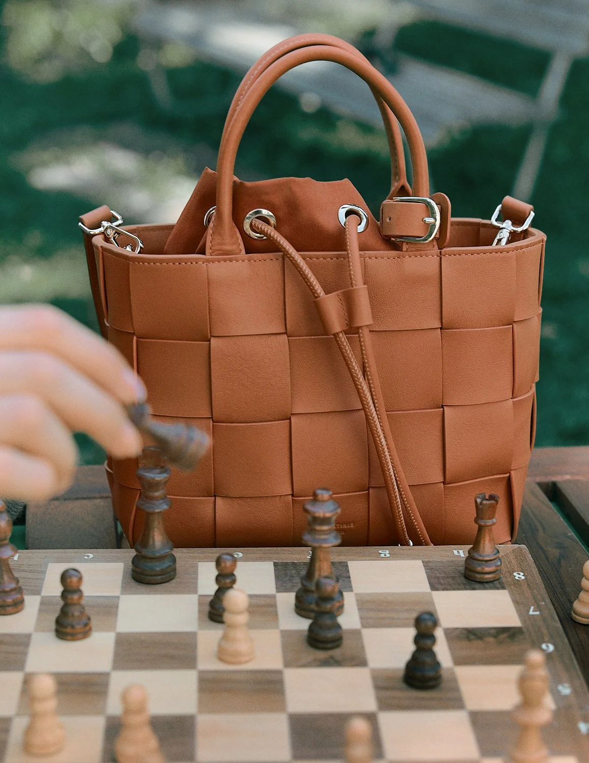 Eine braune Lederhandtasche, die auf einem Schachbrett sitzt, während jemand Schach spielt.