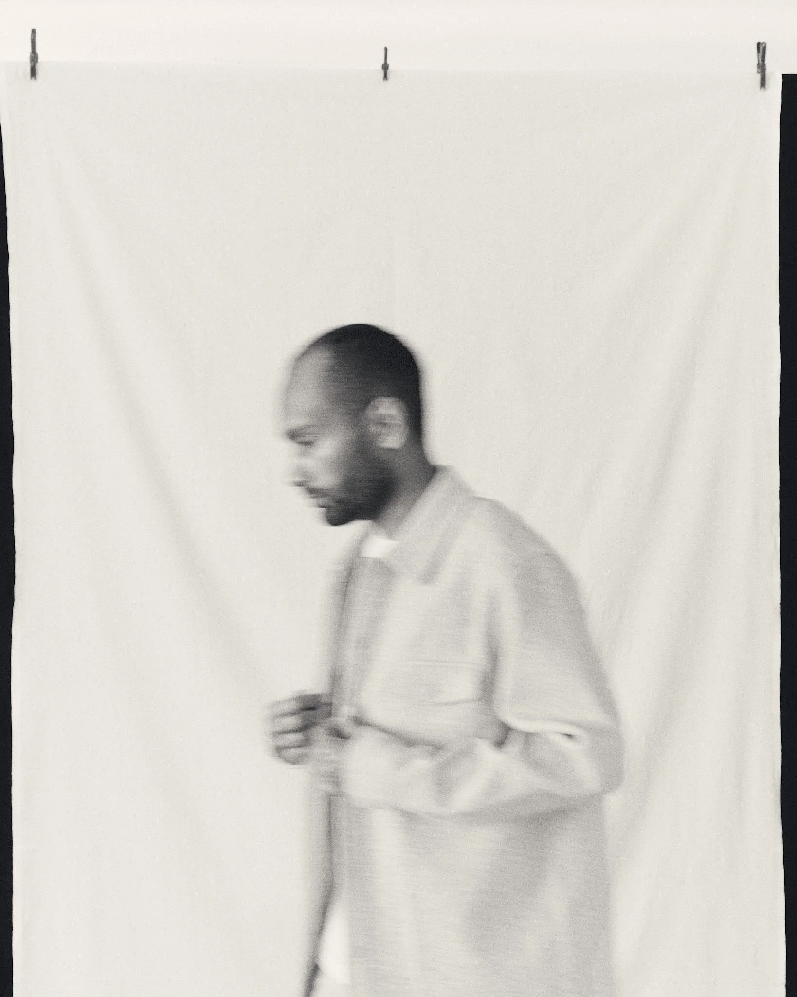 Mann in einem weißen Hemd steht vor einem weißen Hintergrund, die Aufnahme ist leicht unscharf.