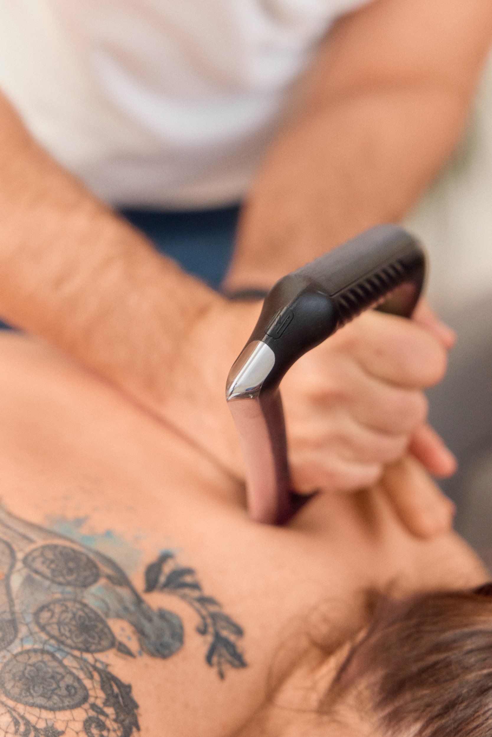 Masseur führt eine Rückenmassage an einem Kunden aus, sichtbarer Tattoo auf Rücken, in einer Behandlungsszene.
