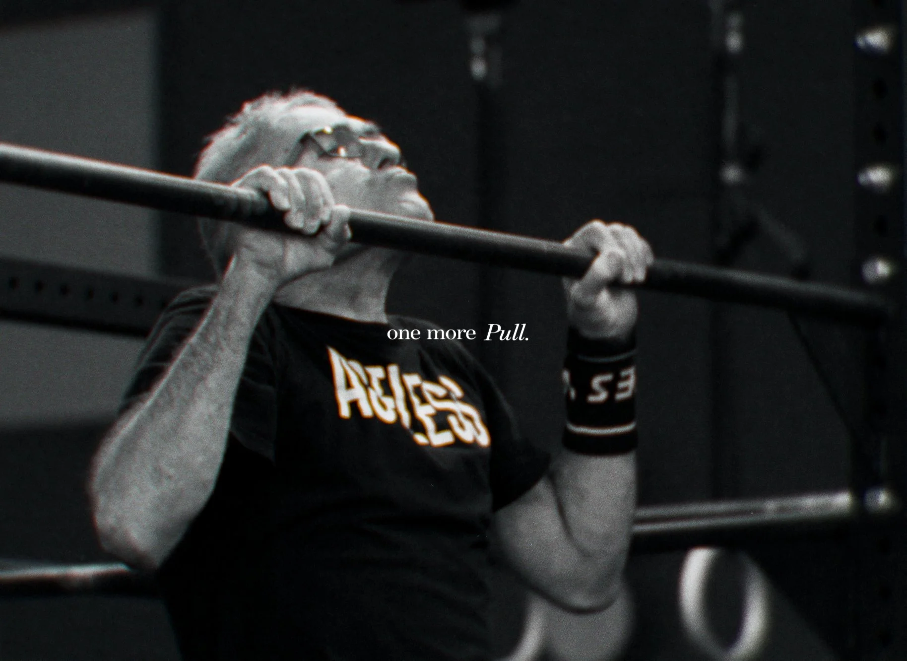 Eine Person hebt eine Stange bei einem Gewichtheben im Fitnessstudio, trägt eine Armbanduhr und eine schwarze T-Shirt mit gelber Schrift. Der Text im Bild lautet 'one more Pull'.