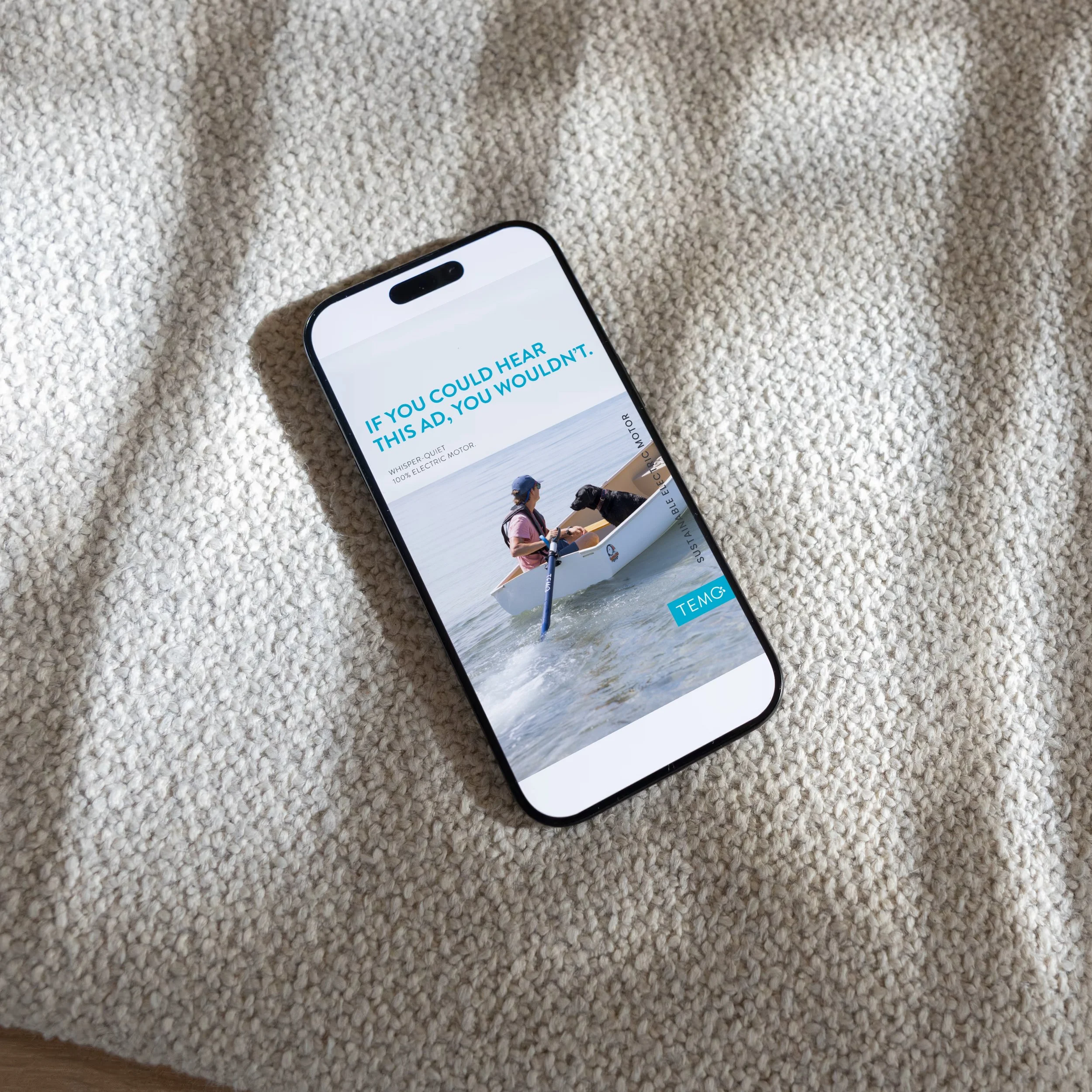 Smartphone displaying an advertisement with a person paddling a canoe, and a text that says 'IF YOU COULD HEAR THIS AD, YOU WOULDN’T.' on a beige textured fabric background.