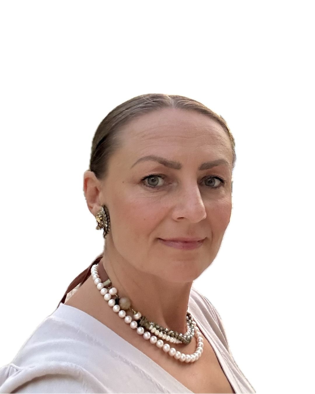 A woman with light skin, grey eyes, brown hair pulled back, wearing earrings and two pearl necklaces, dressed in a white top with a V-neck.