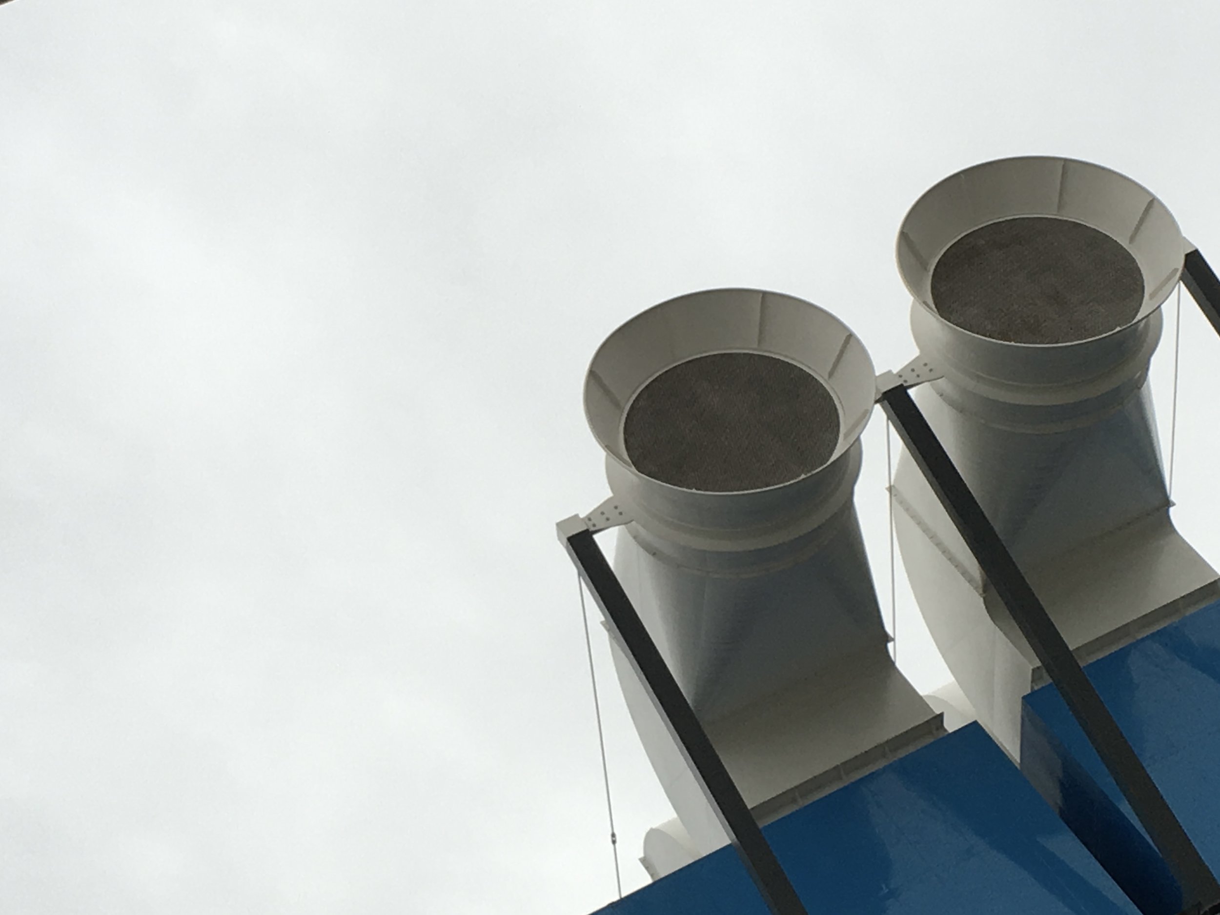 Upward view of two industrial exhaust vents against a cloudy sky