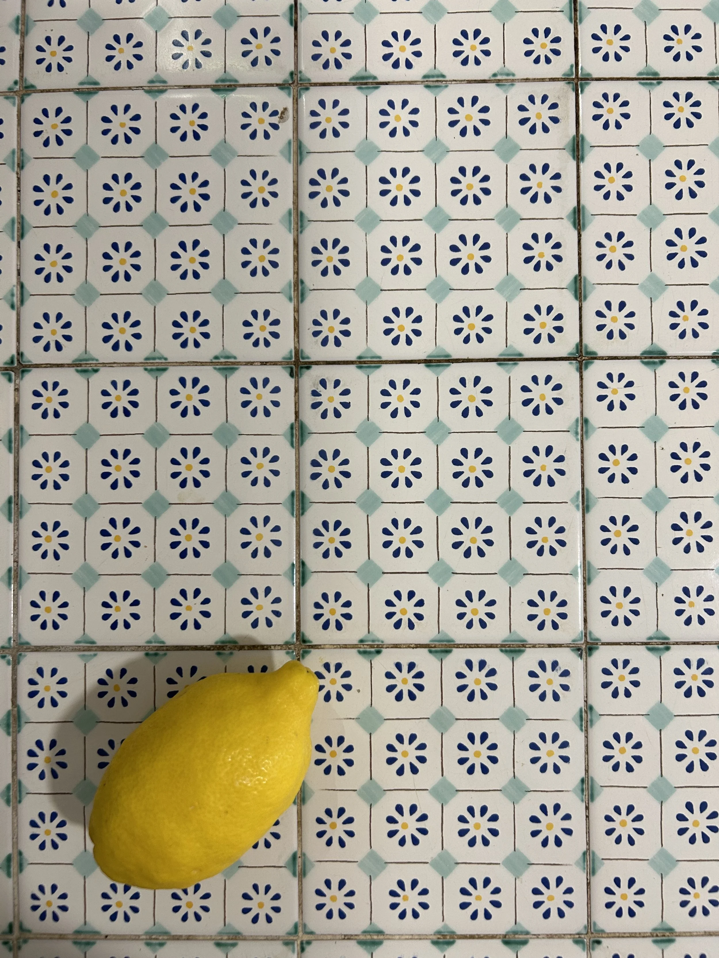 A yellow lemon on a tiled floor with a blue and white floral pattern.