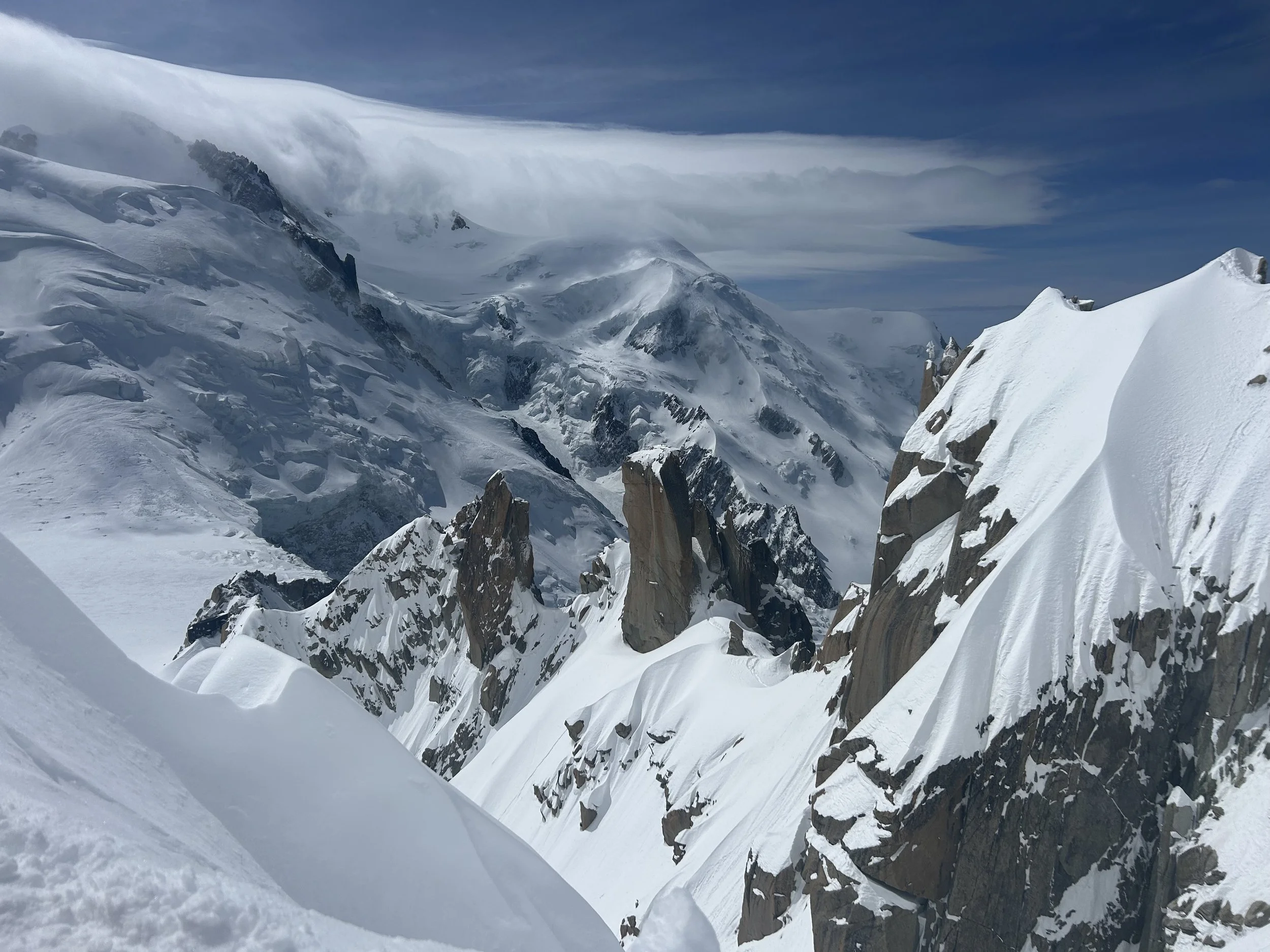 Snow-covered mountain peaks with rocky cliffs, under a cloudy sky.