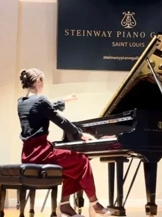 A woman playing a grand piano on a stage in a music hall.