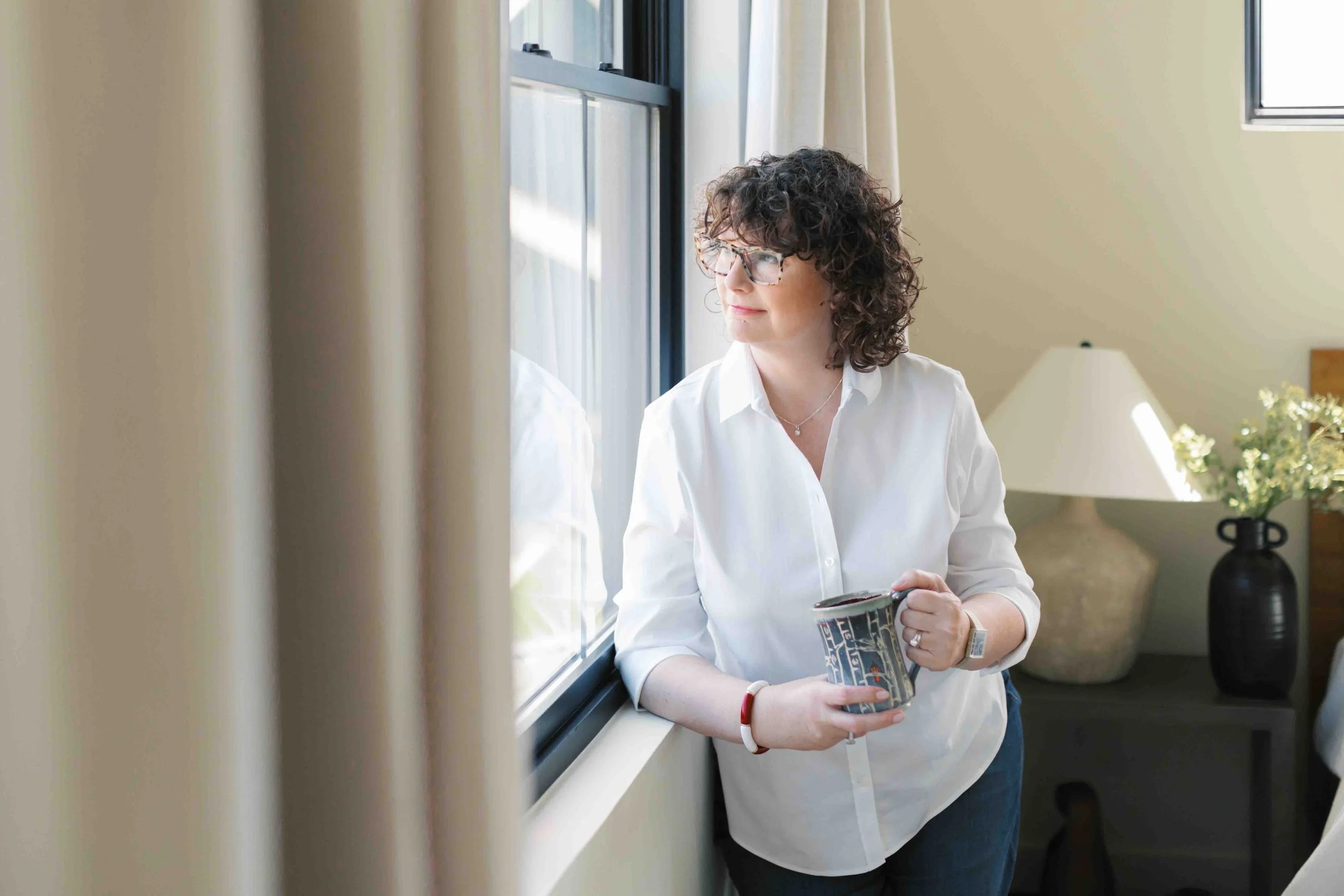 Nichole Alspaugh Williams reflecting by a window with a cup of coffee