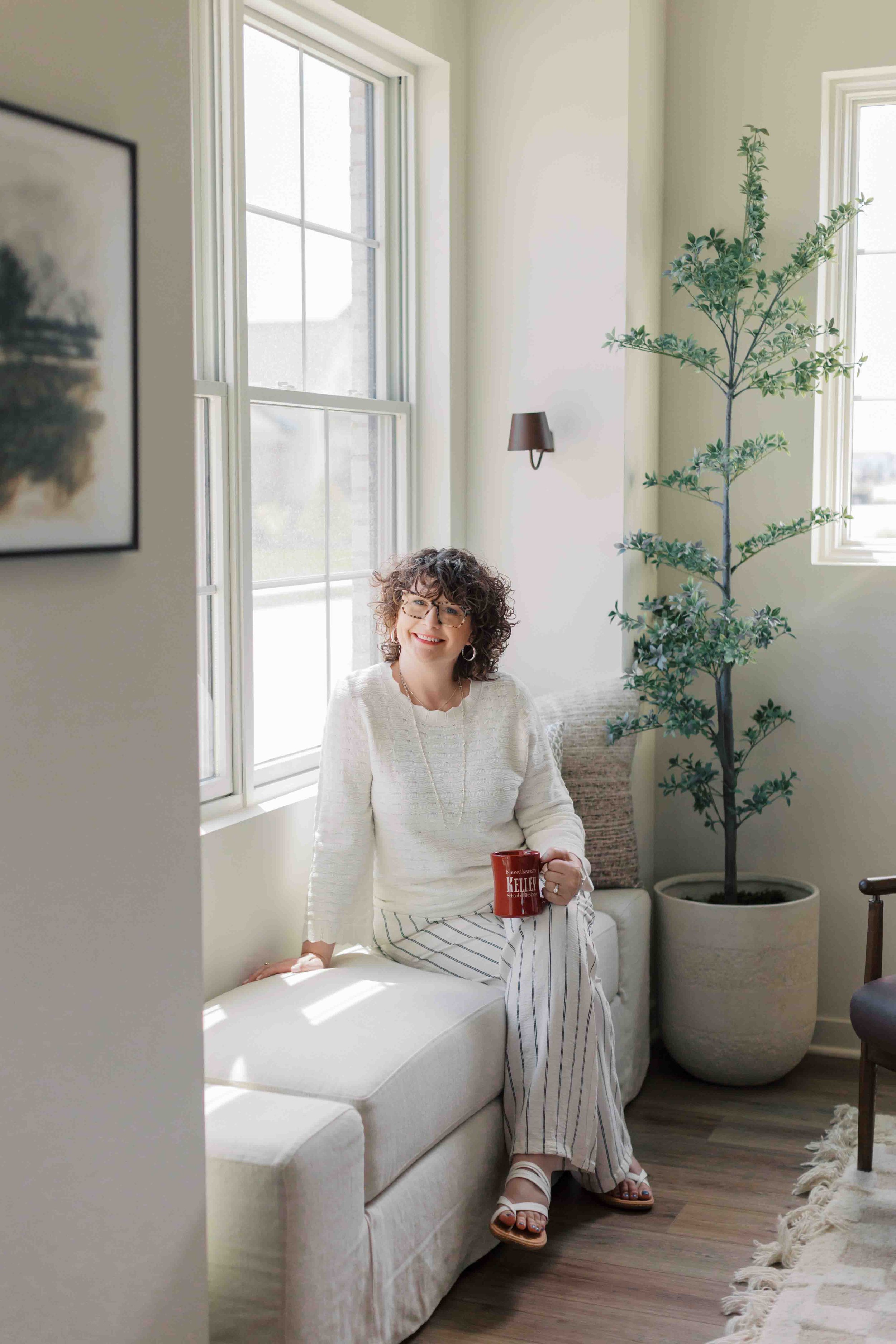 Nichole Alspaugh Therapist smiling and sitting by window with cup of coffee