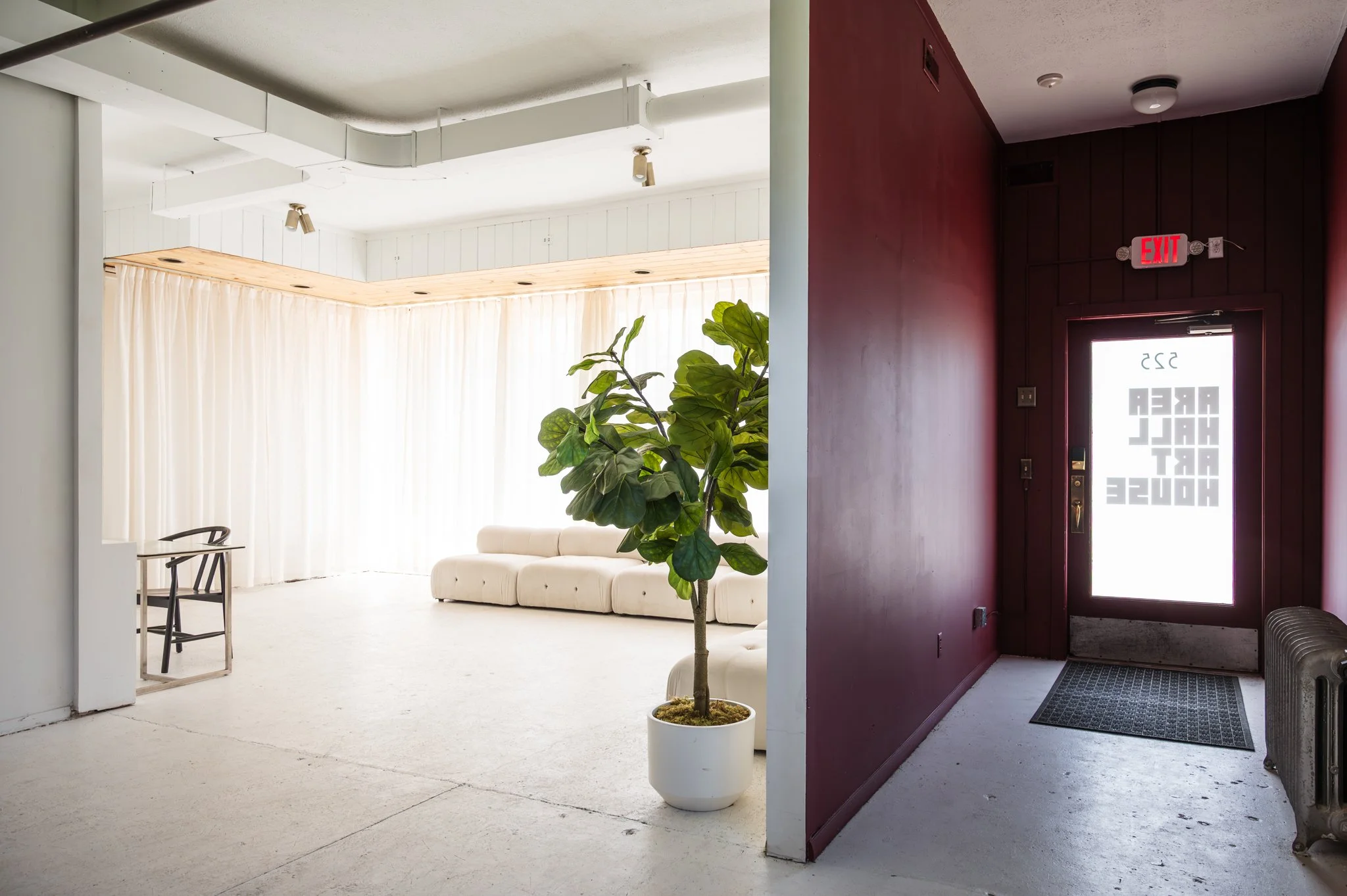 The front area of AH AH's studio white and maroon walls, a white couch, potted plant, and a large window with white curtains.