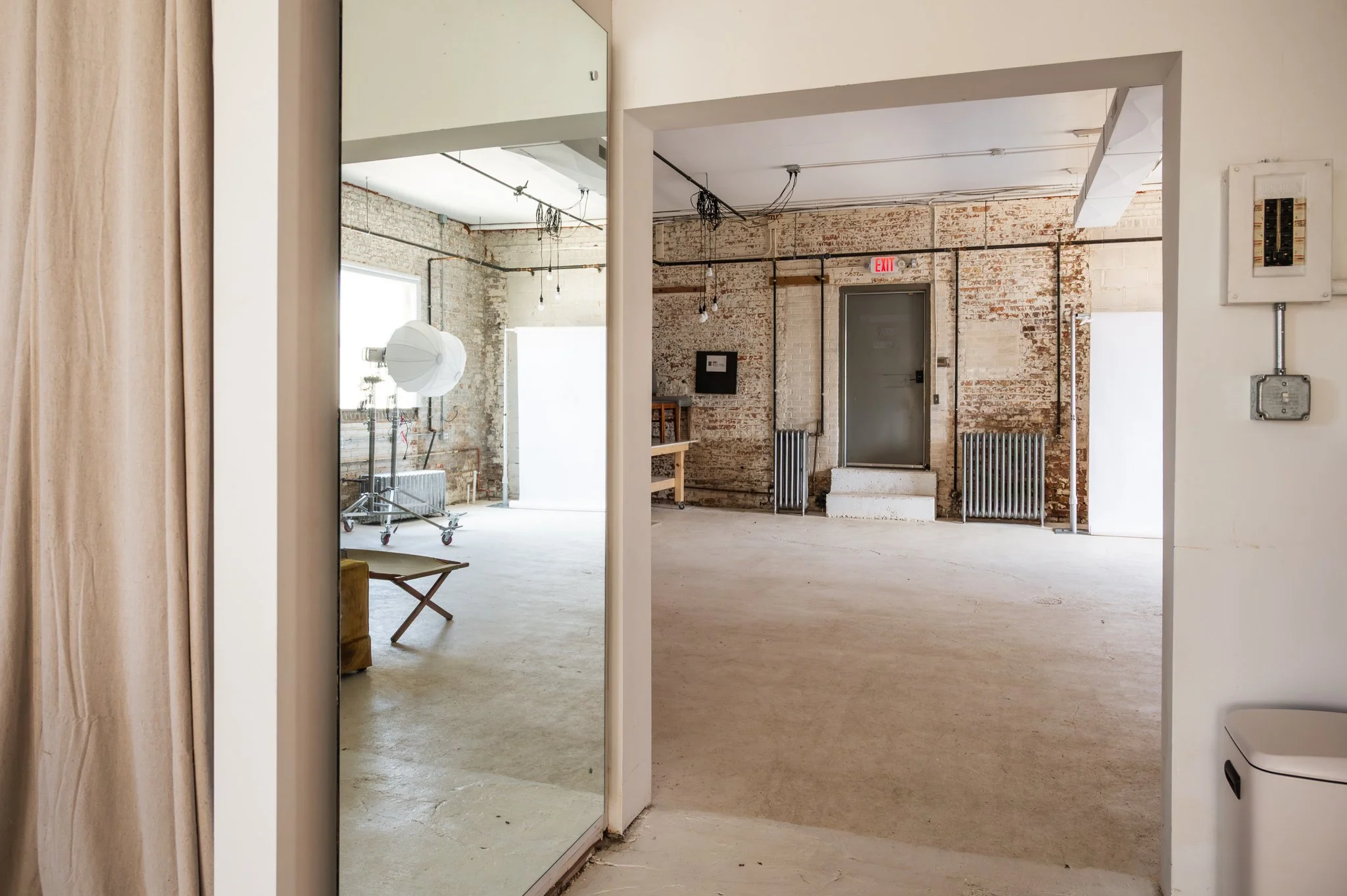 AH AH's industrial-style photo and film studio with exposed brick walls and large windows, a floor to ceiling mirror, and various photo gear and equipment.