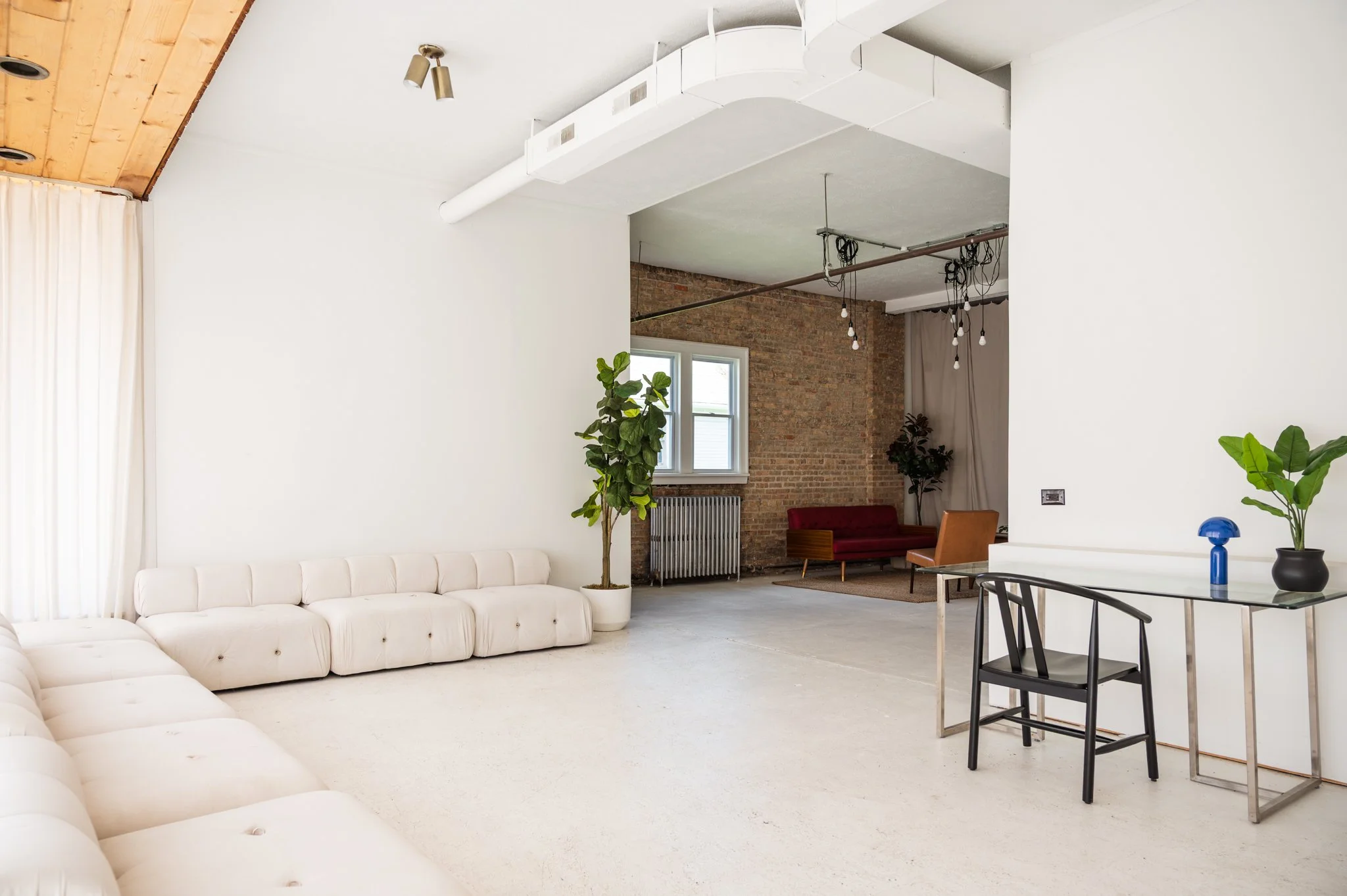 Front studio space with multiple shooting setups including a dreamy modern living room, a clean simple workspace, and a cozy sitting area with exposed brick wall.