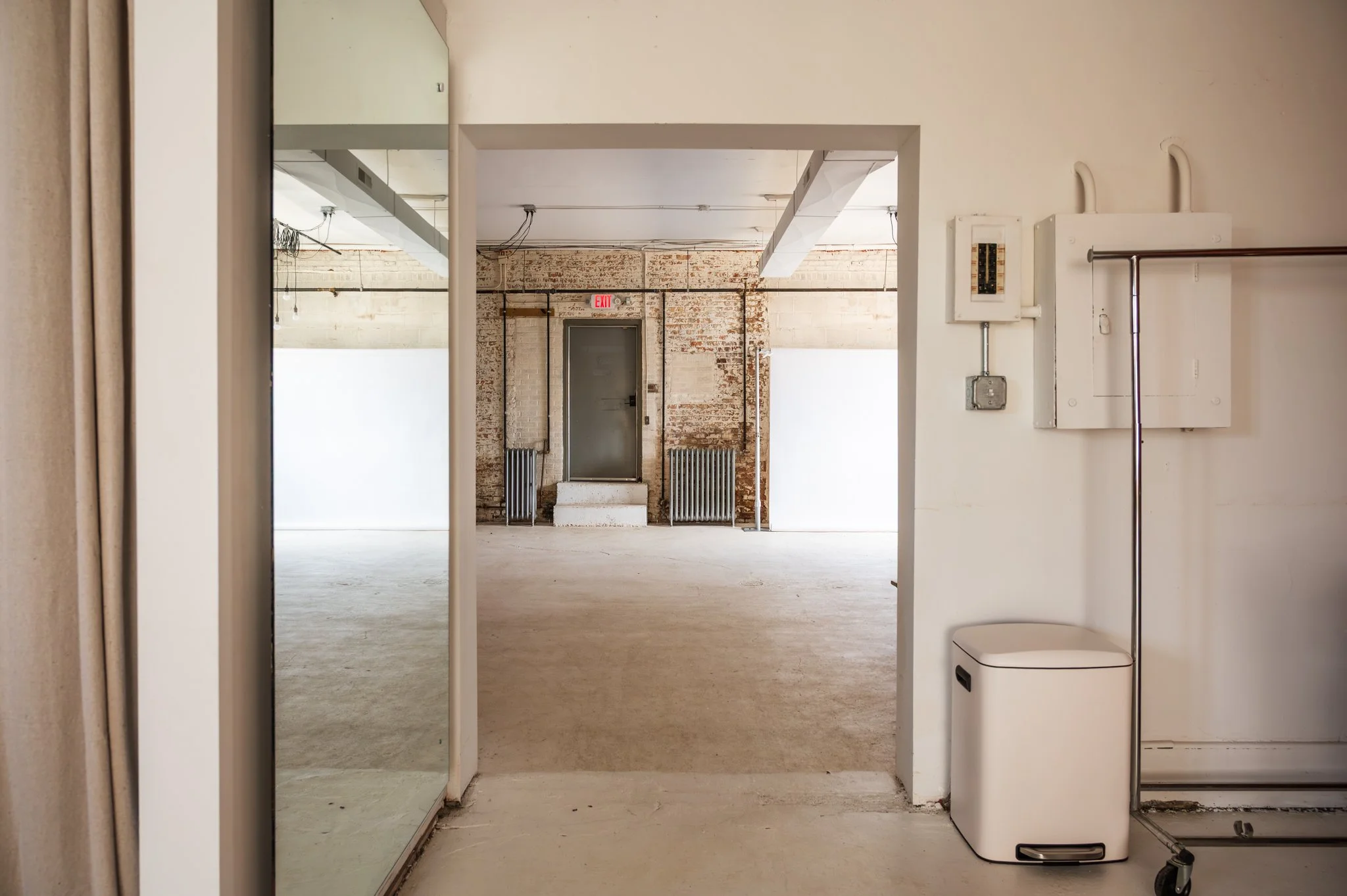 AH AH's industrial-style photo and film studio with exposed brick walls and large windows, a floor to ceiling mirror, and various photo gear and equipment.