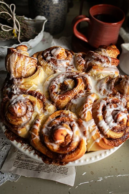 Cinnamon rolls topped with icing served on a white plate, with a mug of coffee in the background.