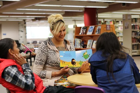 Women reading a children's book to two girls in a library.