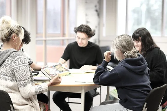 Group of five young adults studying around a table in a bright room.