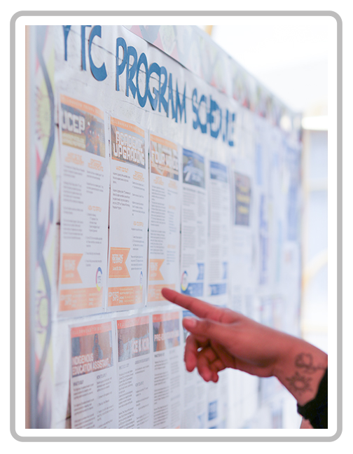 Person pointing at a bulletin board with multiple informational flyers or posters, possibly for a school or community event.