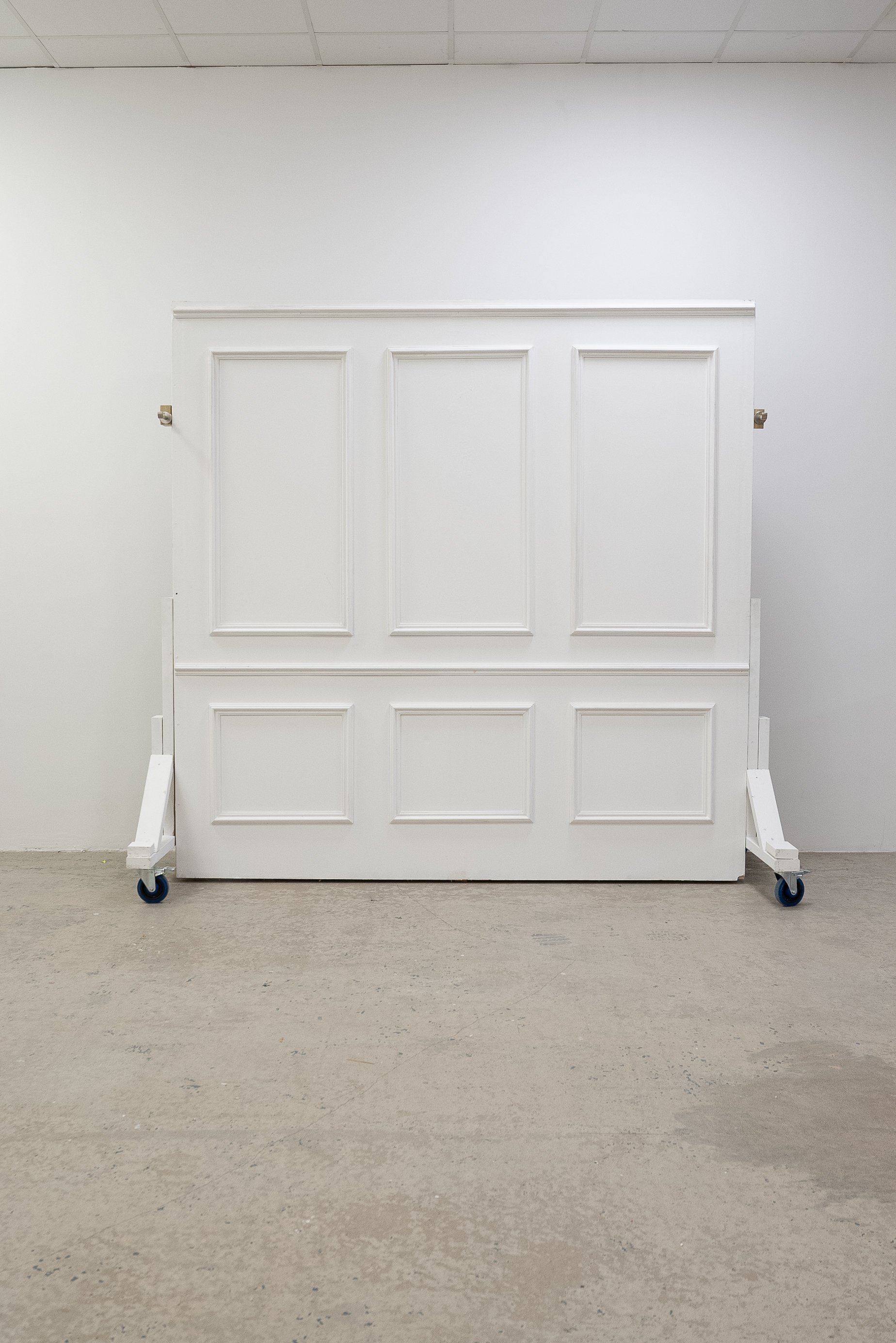 White paneled wall on wheels in an empty room with a tiled ceiling and concrete floor.
