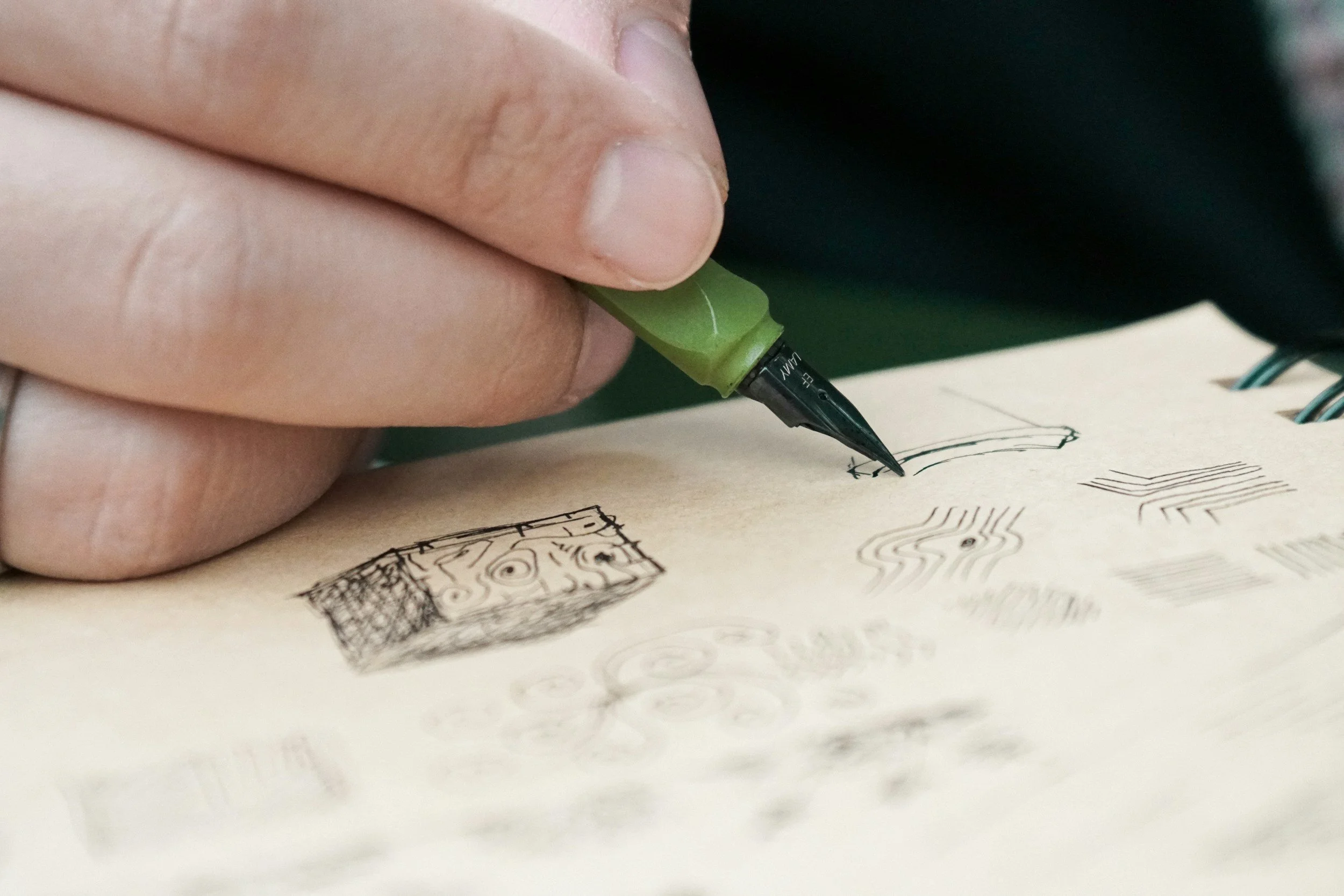 A hand drawing a tiny scribble in a notebook symbolizing micro-moment creative practice.