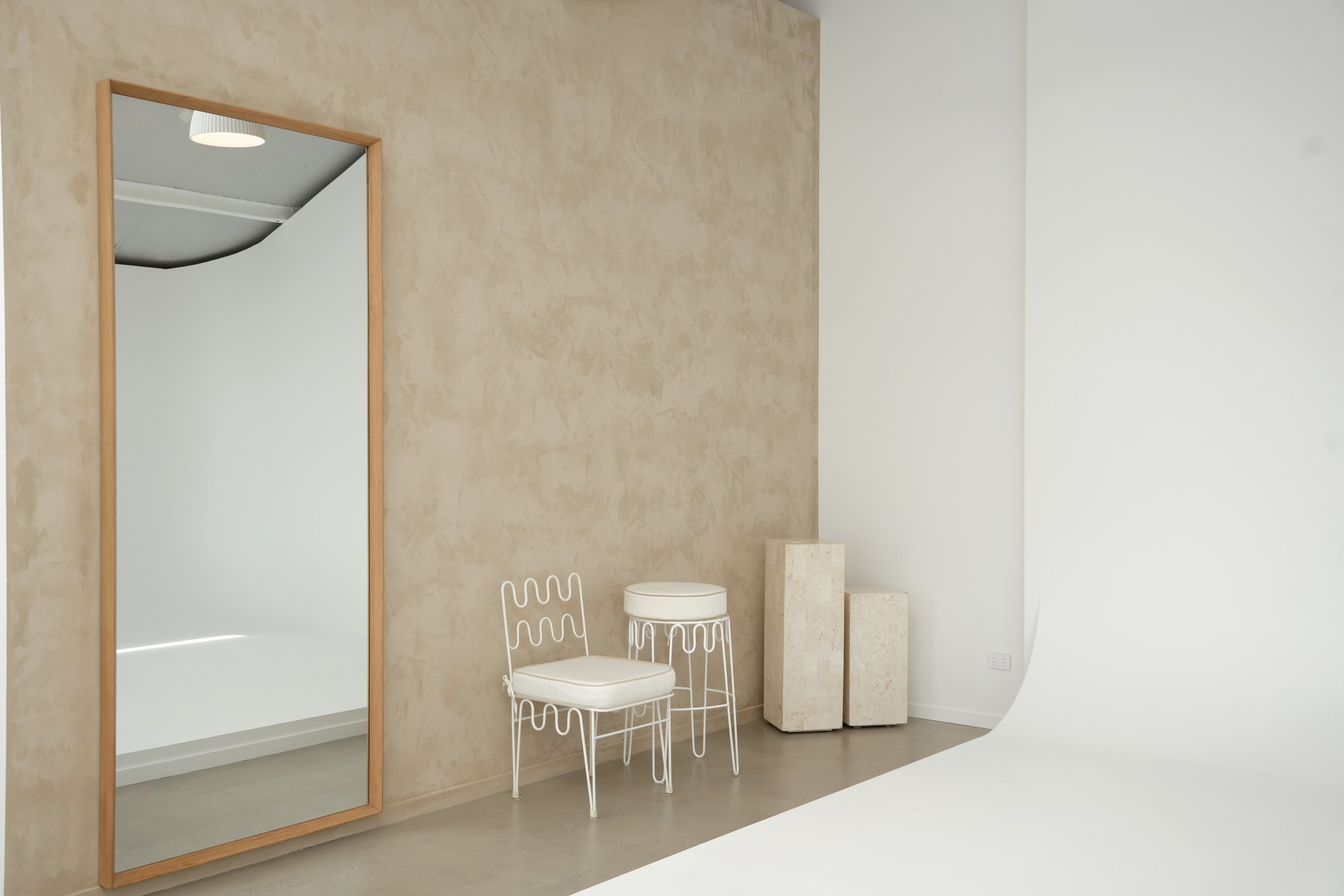 Studio with light gray ceiling, white walls, a white backdrop, three pendant lights, a full-length mirror with a wooden frame, a clothing rack with two white hangers, and a beige wall with a door.