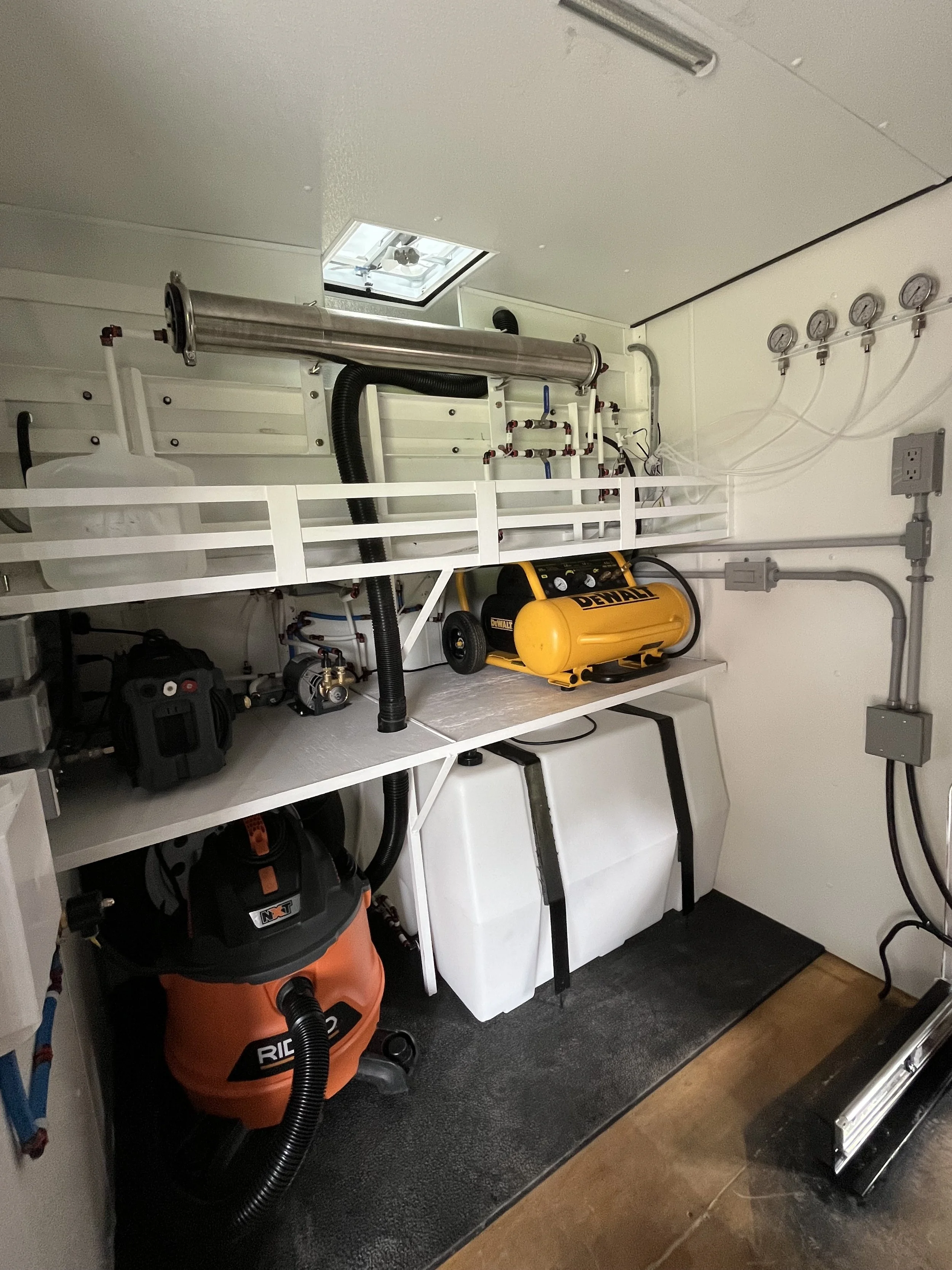Showing inside a mobile detailing trailer where there is a 100 gallon water tank, large vacuum, pressure washer, water pump, air compressor, and a reverse osmosis filter to make spot free water.