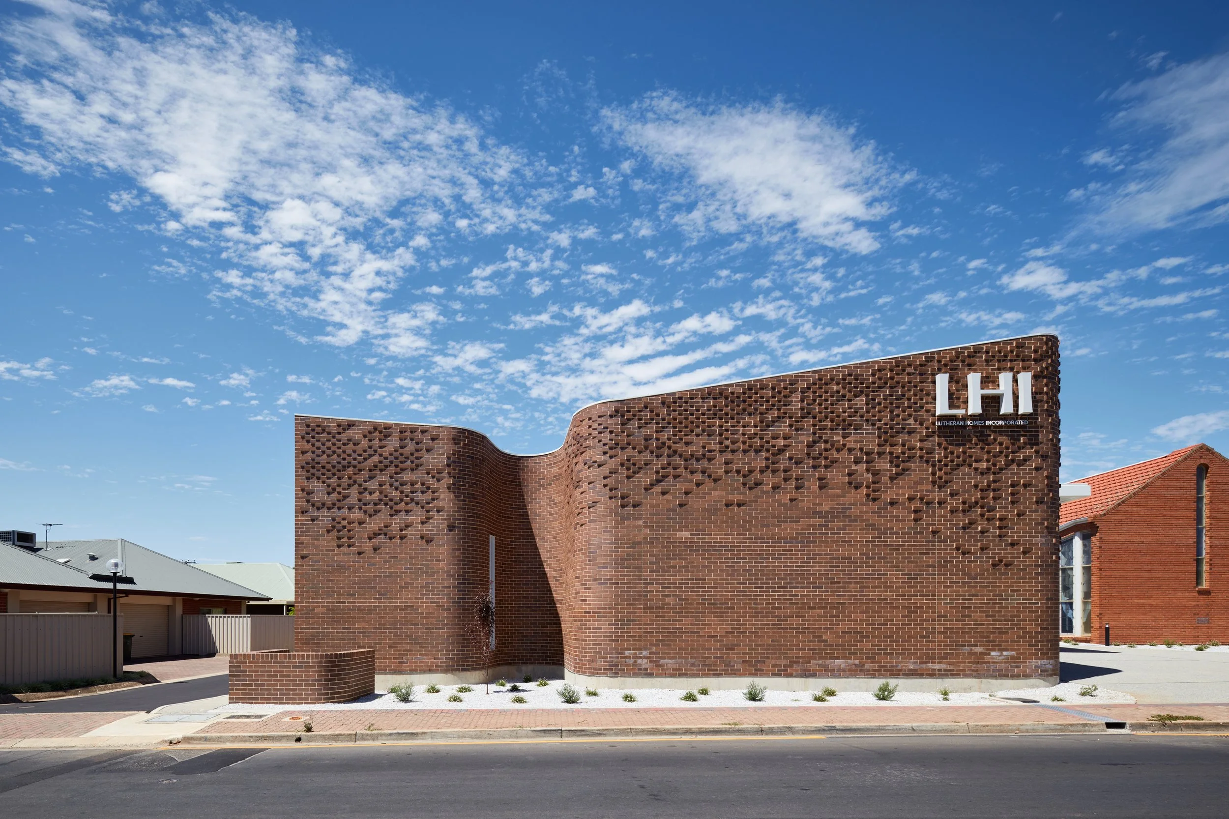 A brick building with a curved wall and white letters 'LHI' on it, under a blue sky with scattered clouds.