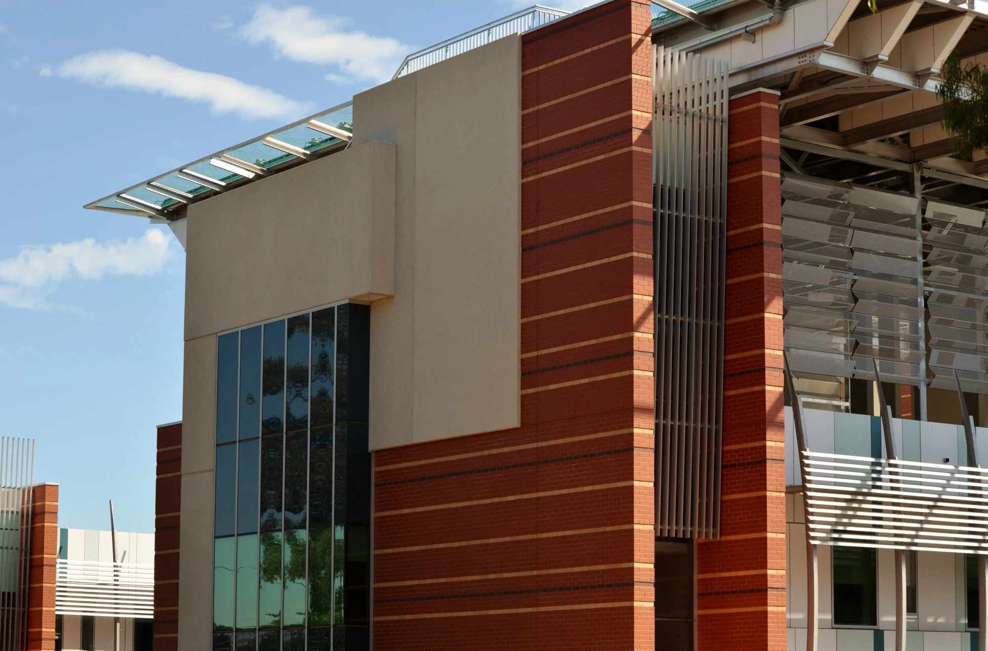 Close-up view of a modern building with a combination of red bricks, white concrete, and reflective glass windows, under a blue sky with a few clouds.