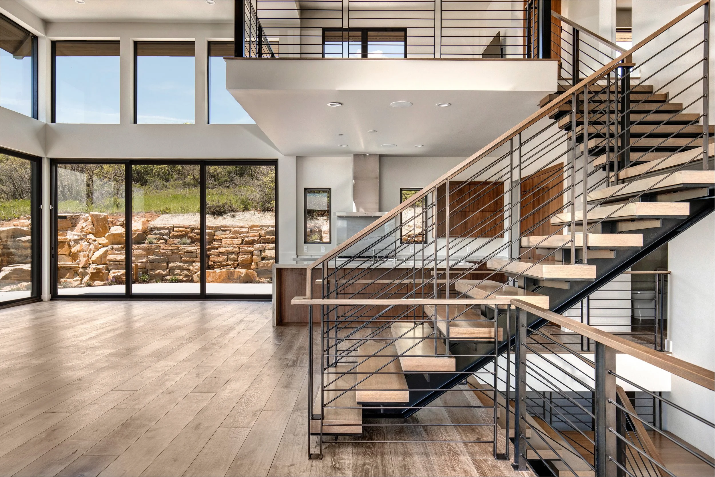 Open living area in the Mountain Ridge Court home, with wide-plank flooring and a metal-and-cable stair.