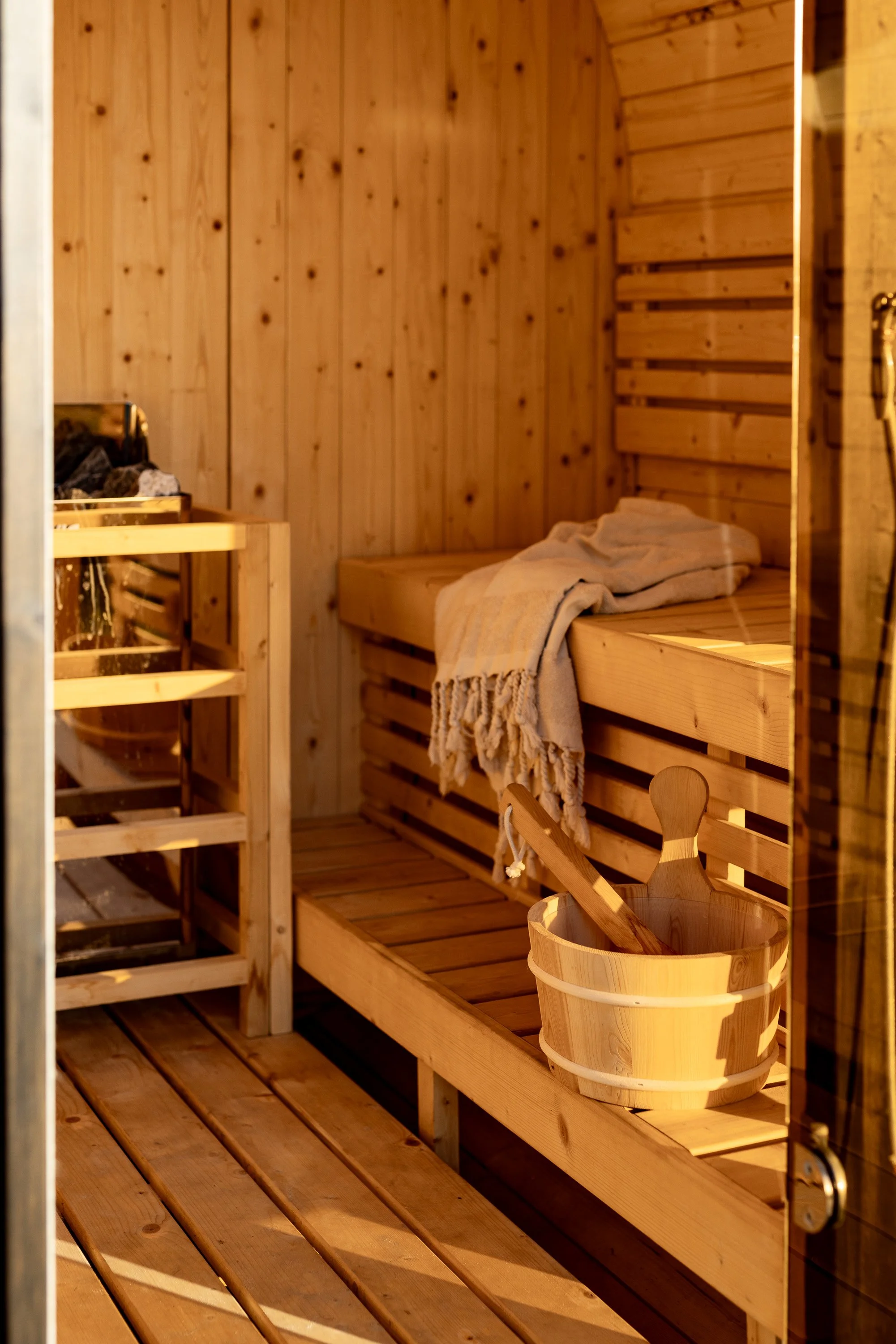 Cooinda on the beach Interior of a wooden sauna with a bench, a towel, a wooden bucket with a ladle, and a small wooden table in a beachfront luxury accommodation.