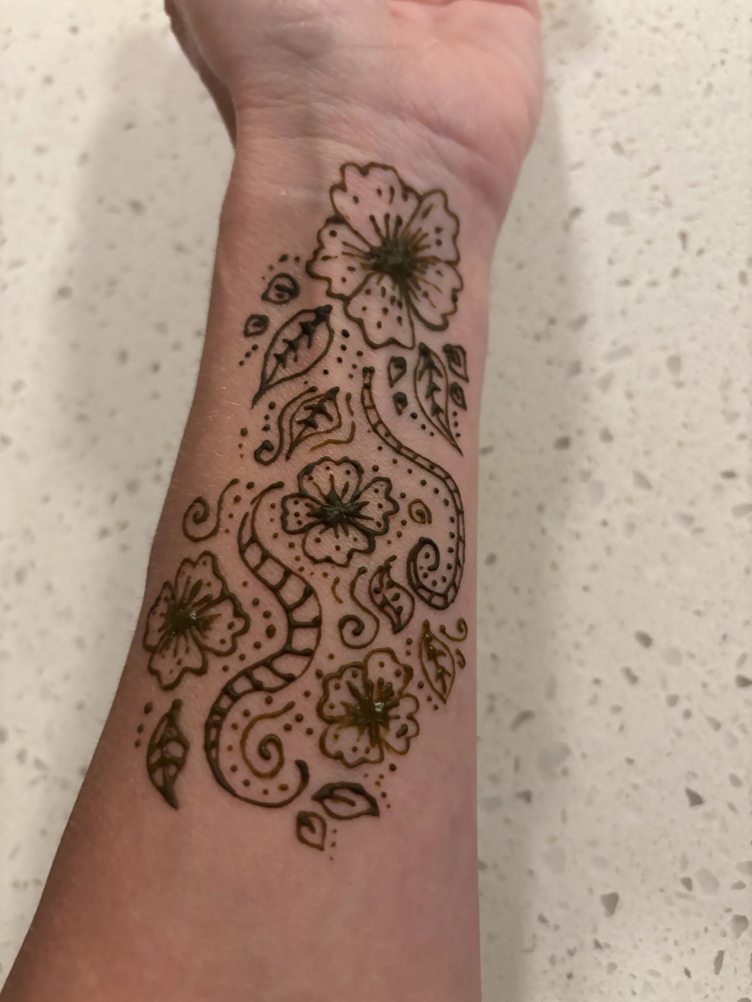 image of the inside of a woman's forearm with a henna designs of multiple flowers and swirls and leaves in a dark brown henna stain